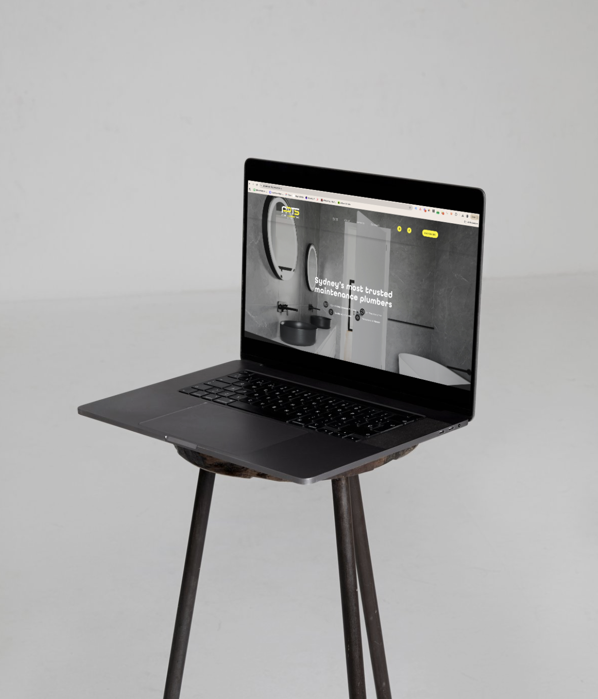 A laptop on a wooden stool displaying a website for maintenance plumbers in Sydney.