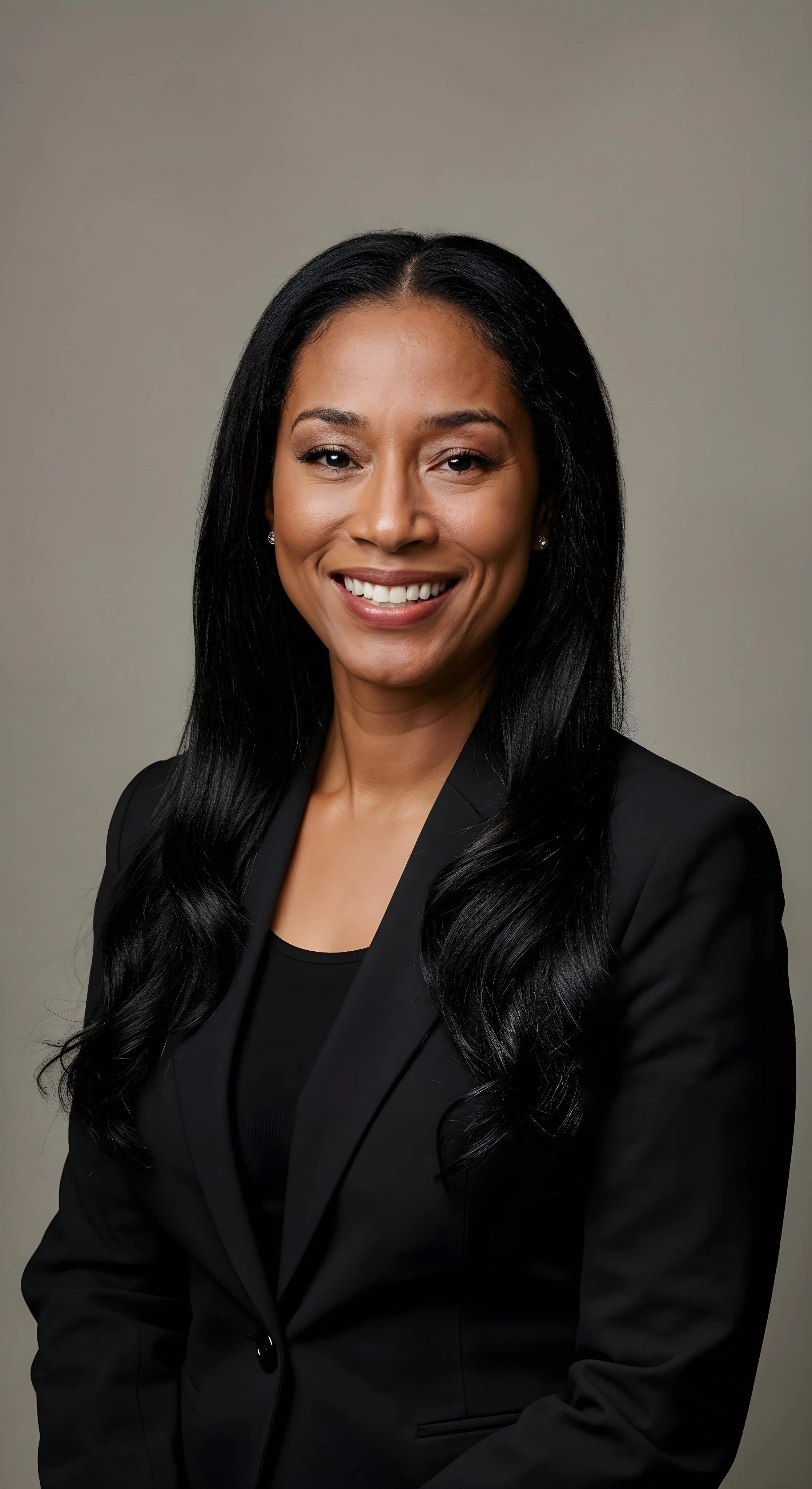 A professional woman with long black hair smiling in a black blazer and black top against a plain background.