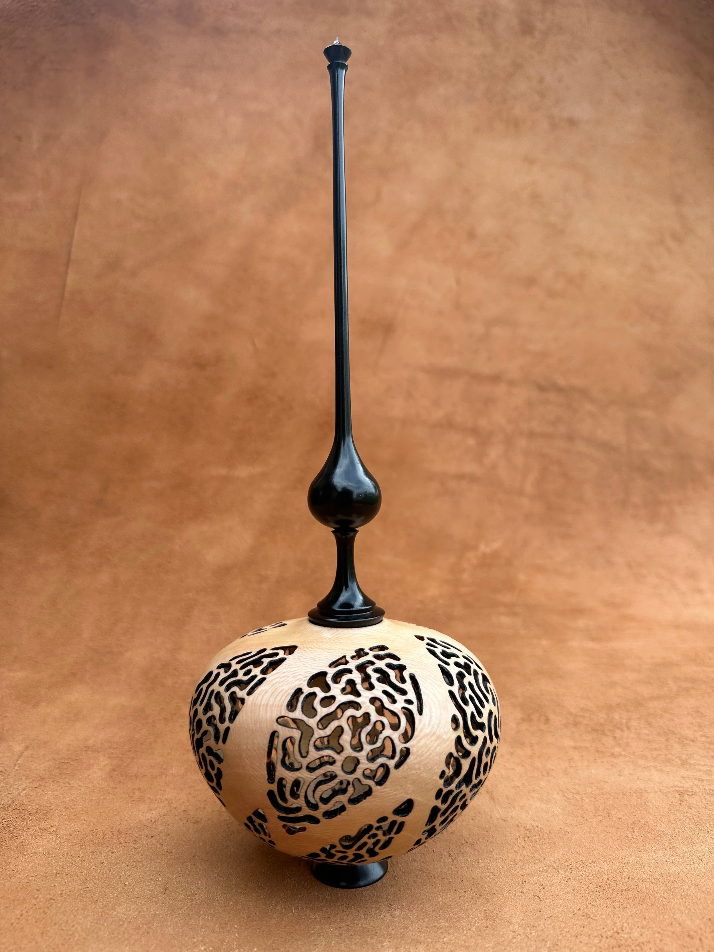 A decorative vase with an intricate black pattern on a light-colored surface and a vertical black handle extending from the top.