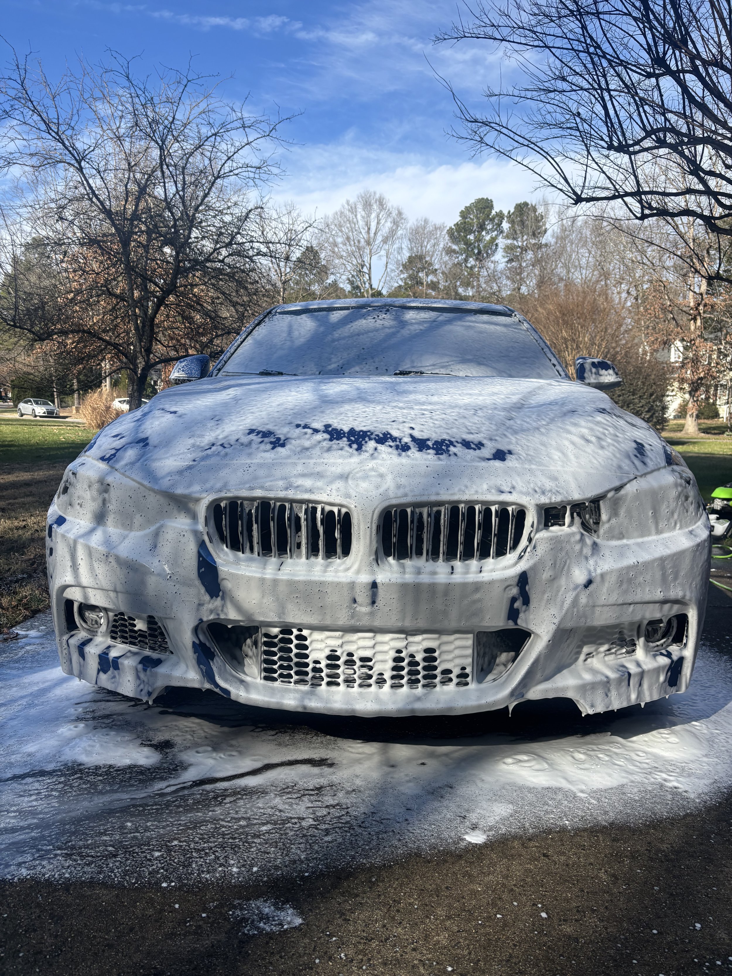 Car covered in soap foam during a car wash outside on a clear day.