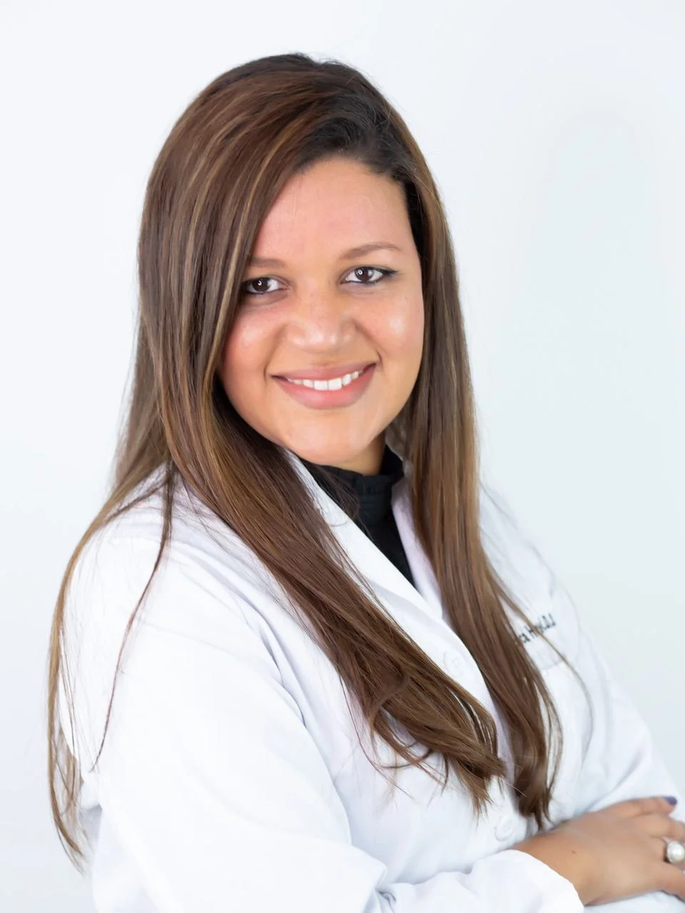 A woman with long brown hair and a white lab coat smiling against a plain white background.