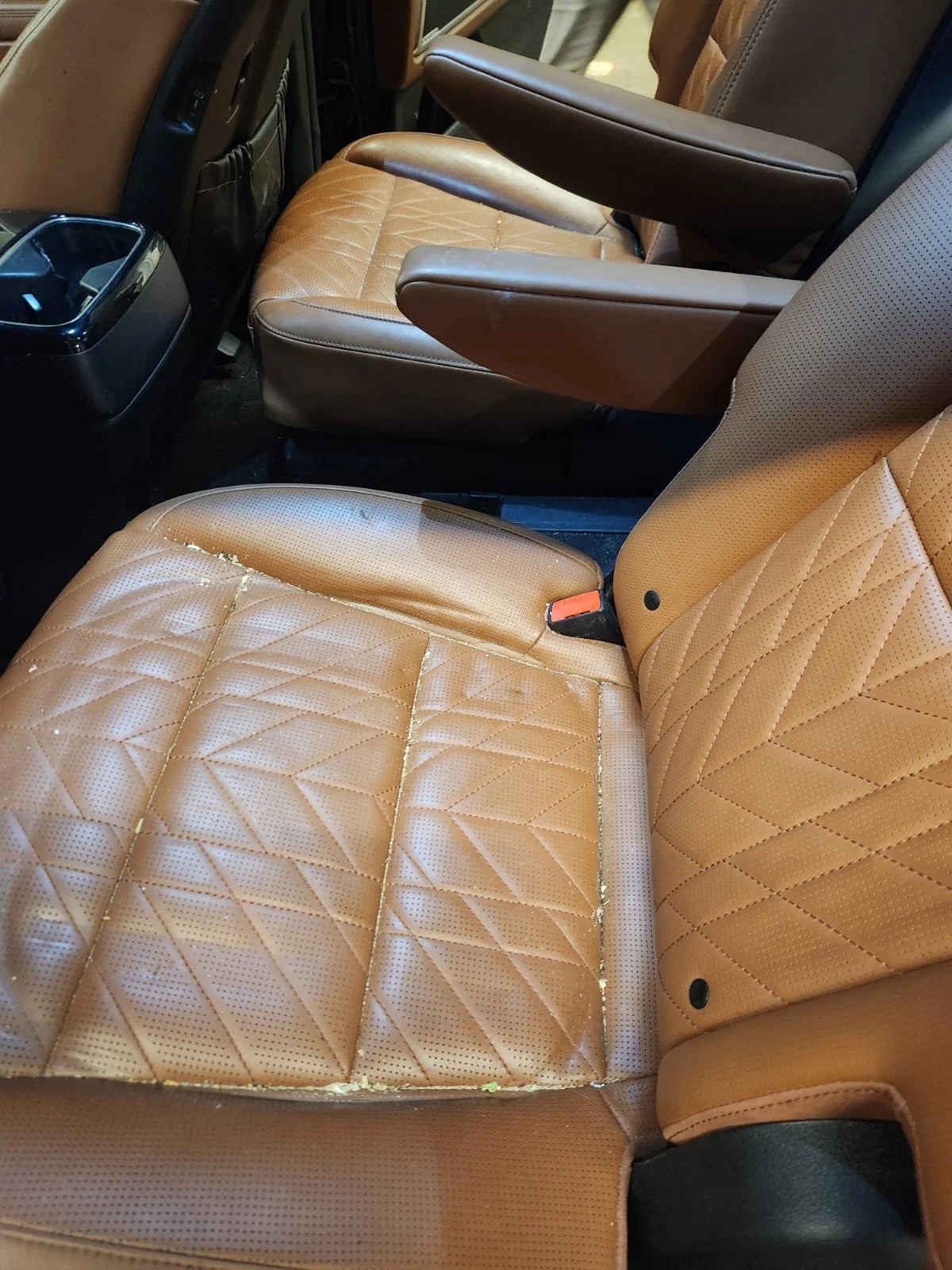 The image shows the interior of a vehicle with tan-colored, diamond-stitched leather seats, one of which appears worn and peeling.