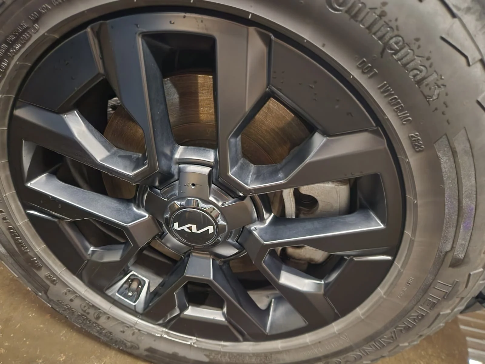 Close-up of a black alloy wheel with a Kia logo on the center cap, mounted with a tire.