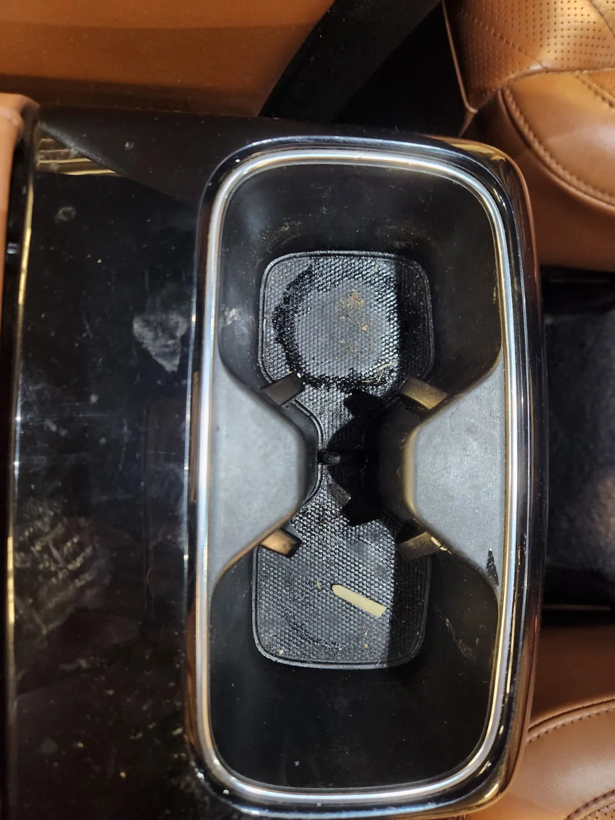 Empty black and silver car cup holder with a textured surface, surrounded by a black dashboard and beige seats.