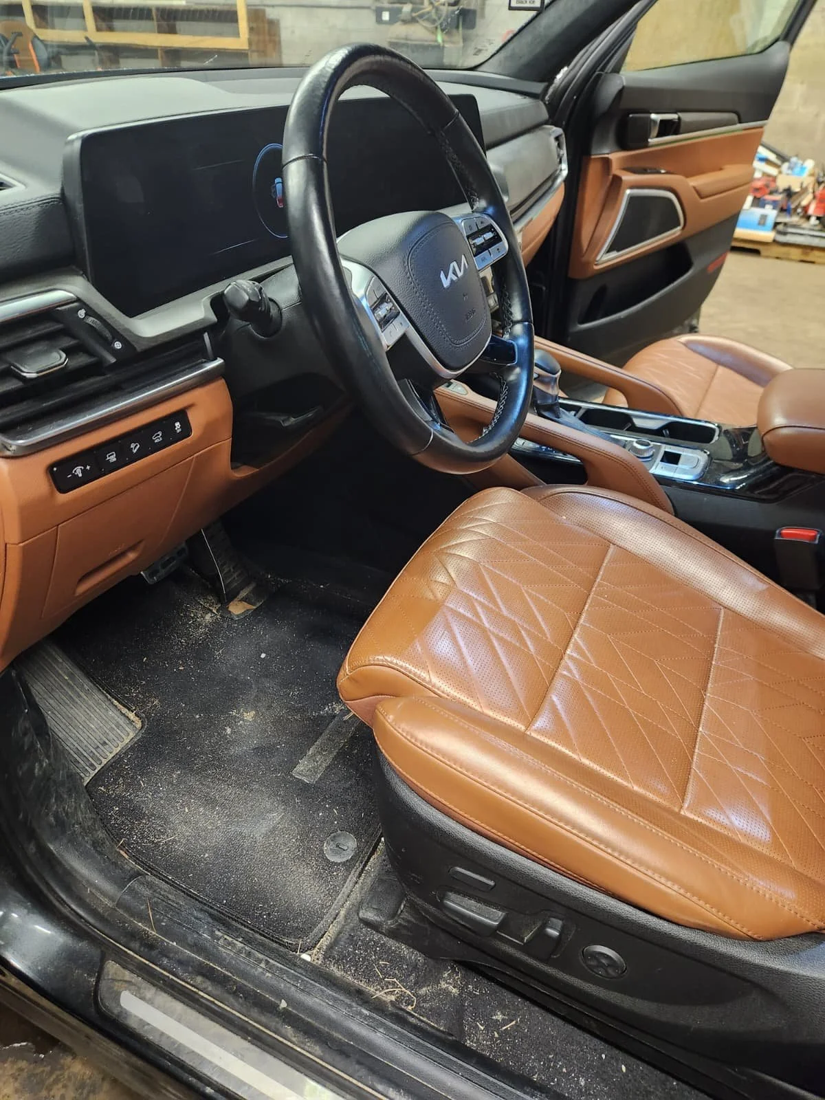 Interior of a Kia vehicle with tan leather seats, a black steering wheel, dashboard, and center console, parked in a garage.