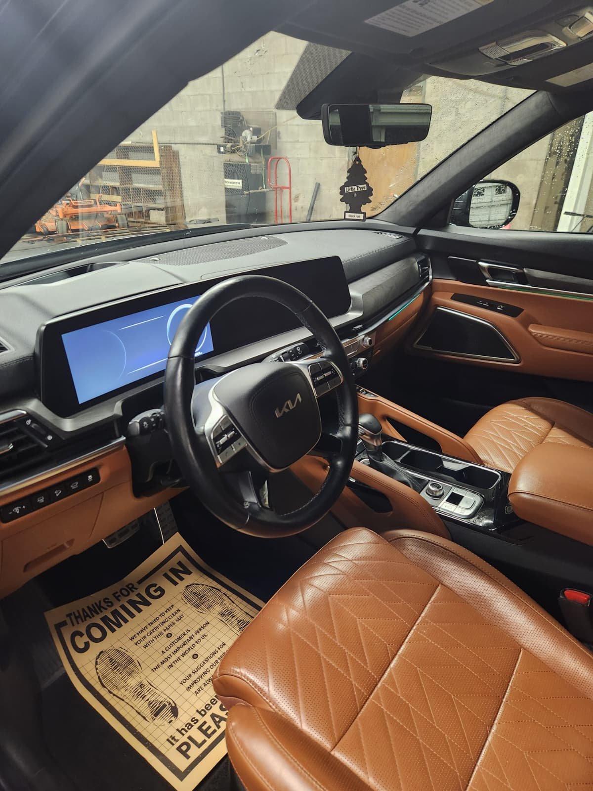 Interior of a vehicle with a digital dashboard, tan leather seats, and a steering wheel with the Kia logo.