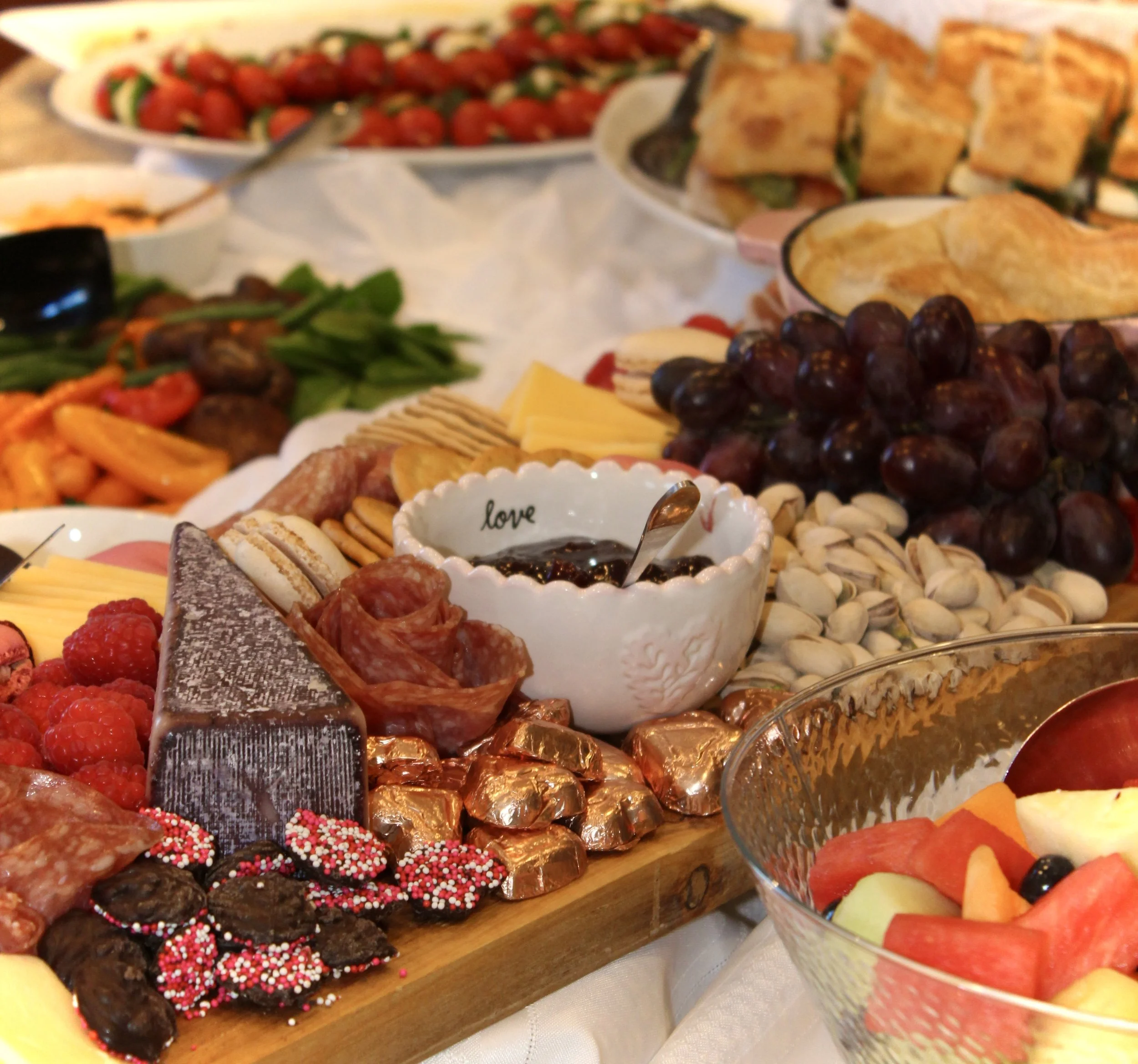 A dessert table with assorted treats including chocolates, cookies, and fruit, decorated with colorful sprinkles and placed on a wooden surface.