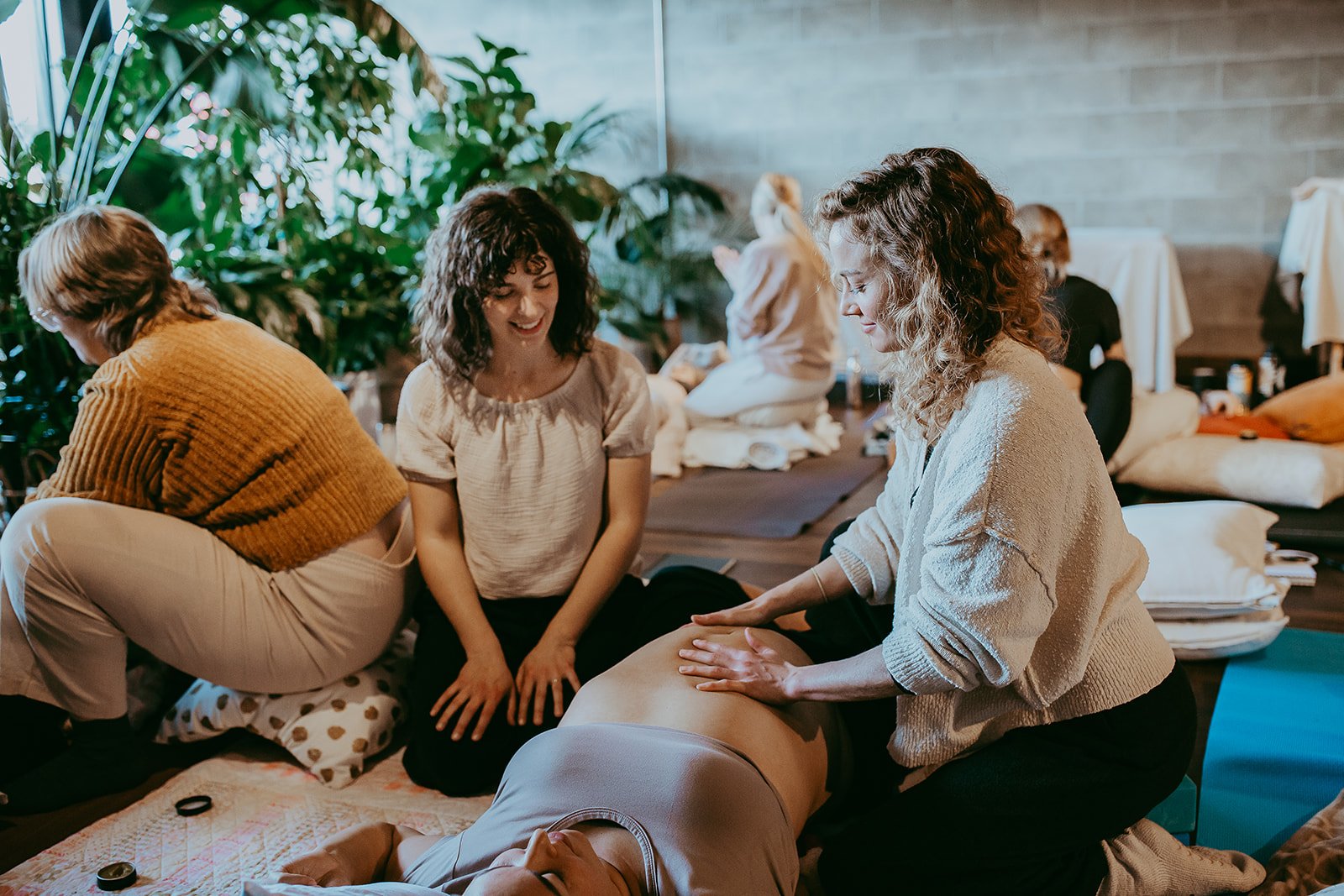 Women practicing reiki or energy healing in a wellness setting with lush plants and natural light.