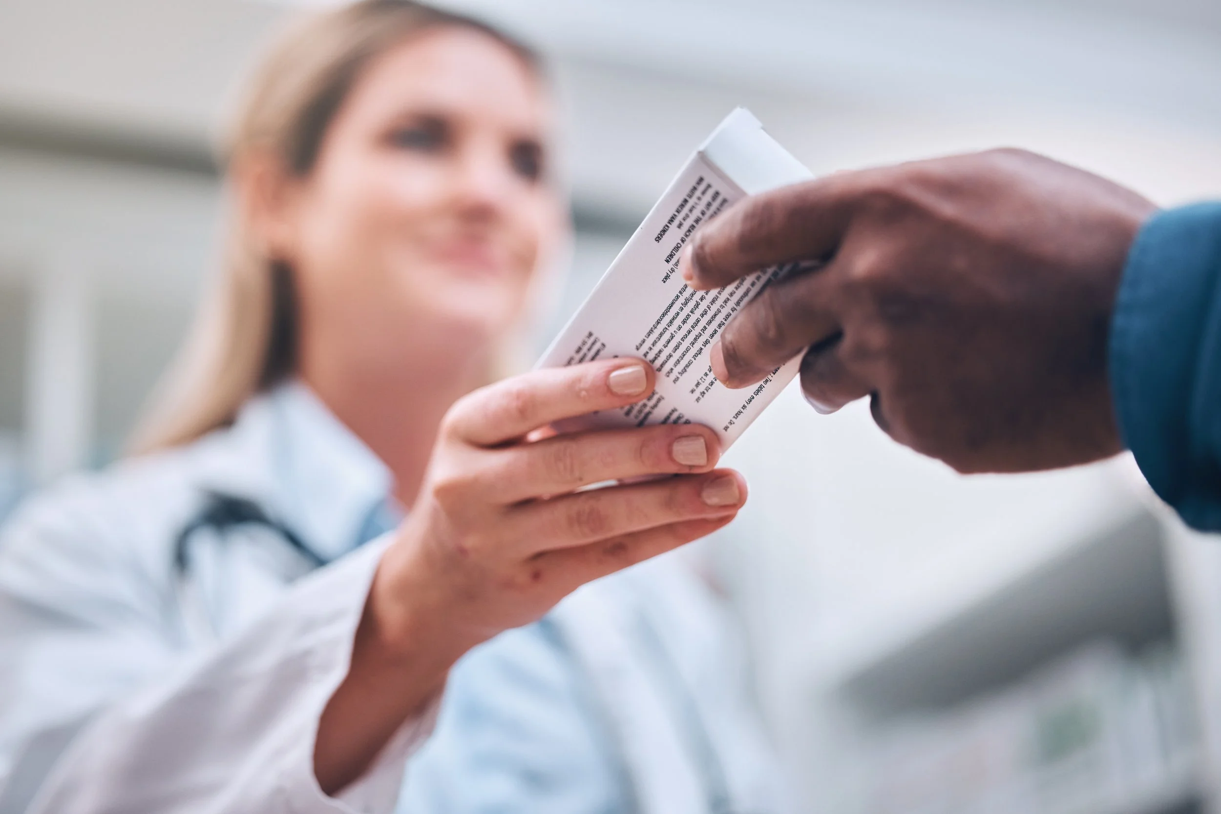A healthcare professional handing a medication box to a patient in a medical setting.