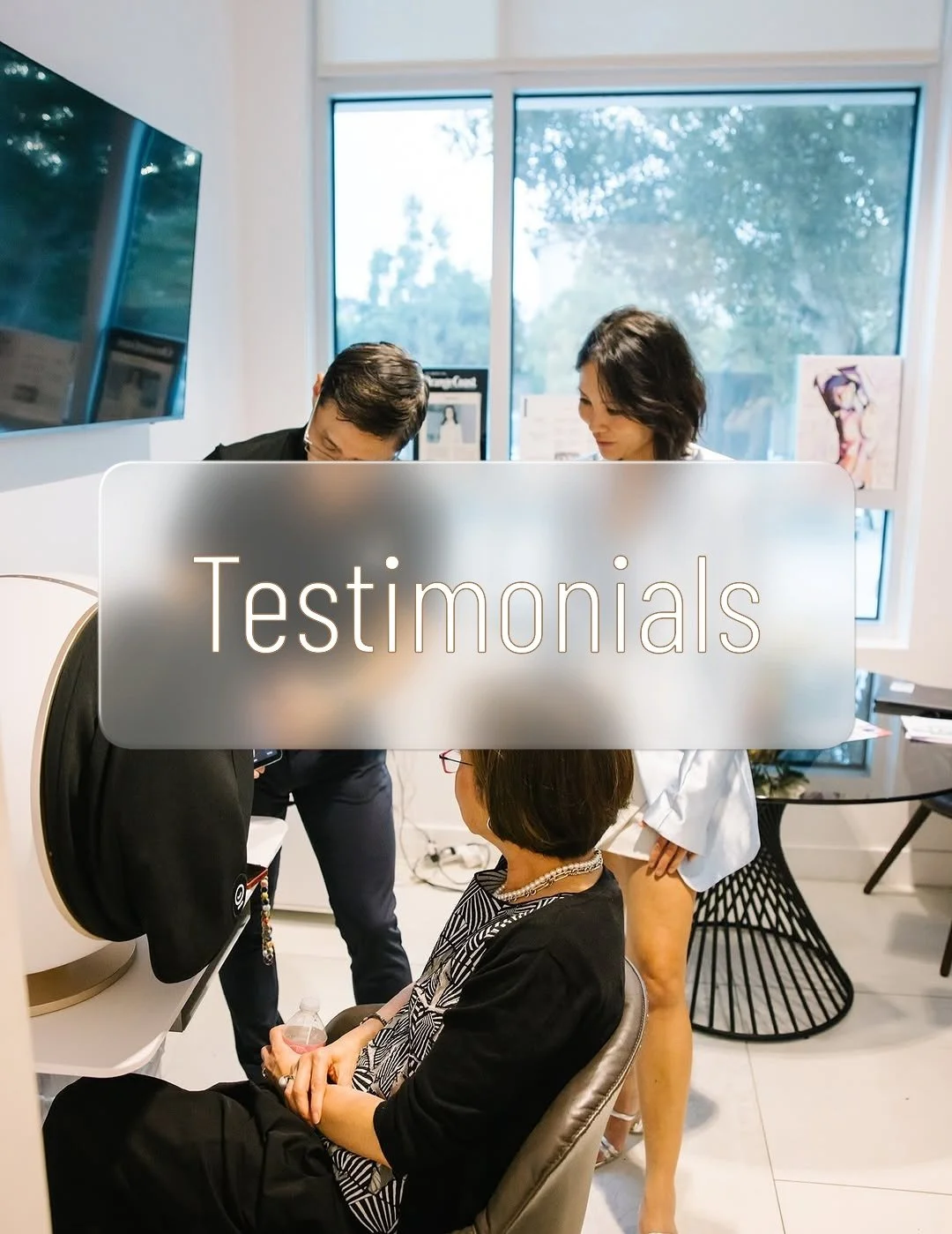 A woman seated receiving a skin and facial analysis, with two people standing and engaging with her in a consultation at a MedSpa, in a modern office, with a large sign that says 'Testimonials' in the foreground.