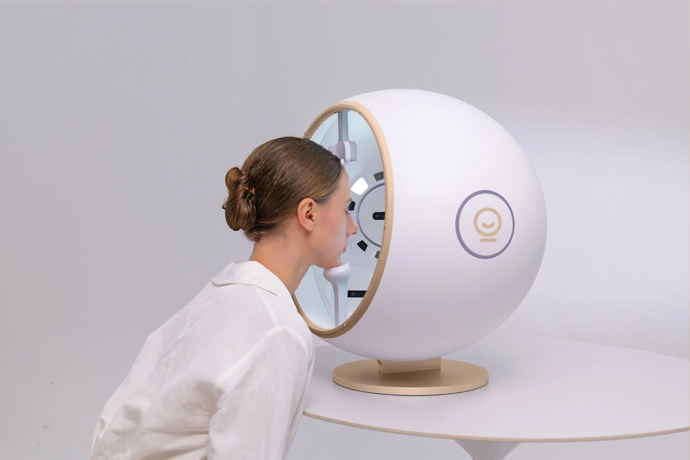 A woman with brown hair in a bun looking into a medical imaging machine, in a neutral room.