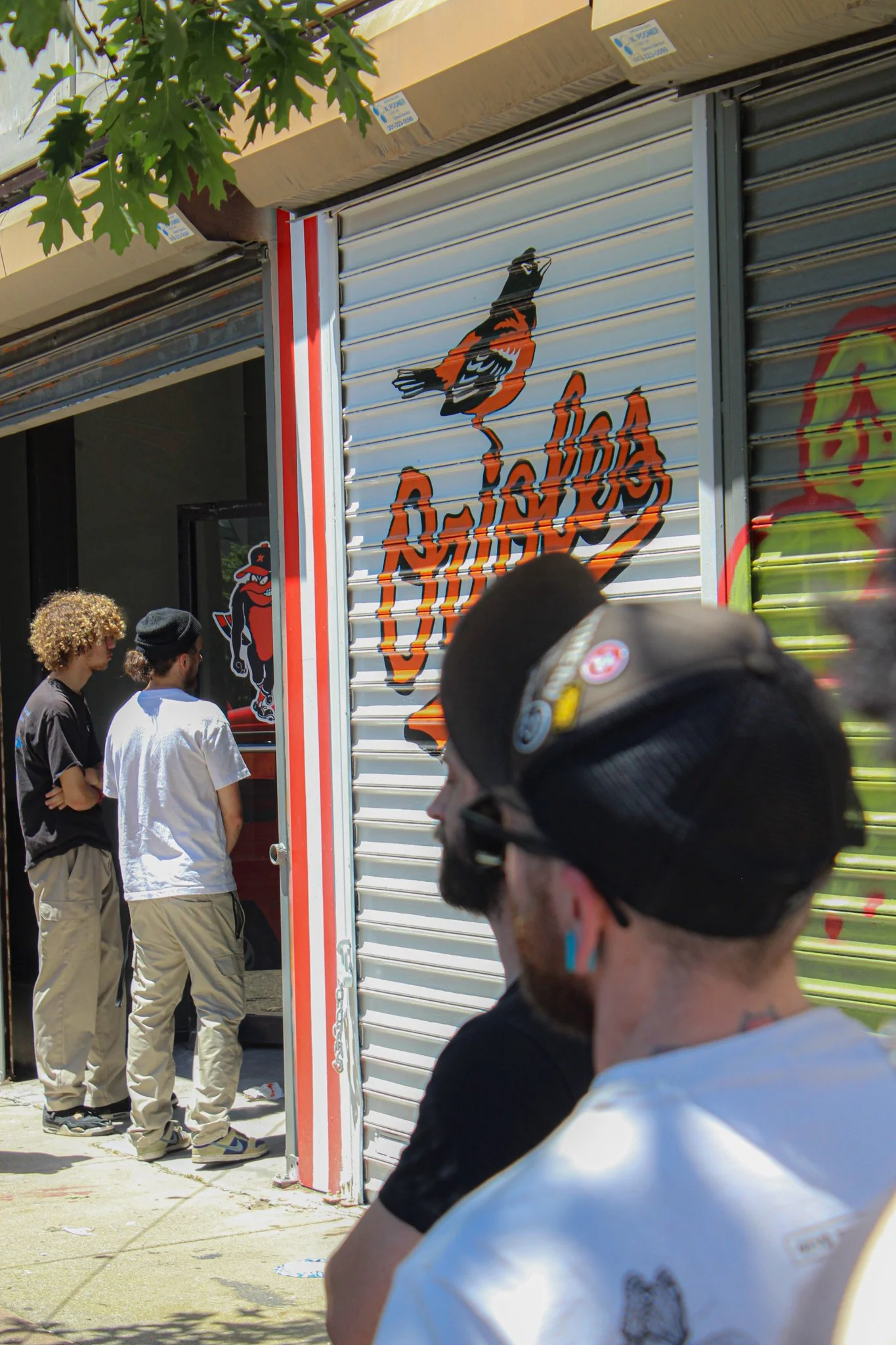 People standing outside a closed store with a roller shutter decorated with a colorful mural of The Baltimore Orioless