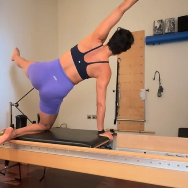 Paula Uribe woman performing side exercise on a Pilates reformer machine in a fitness studio.