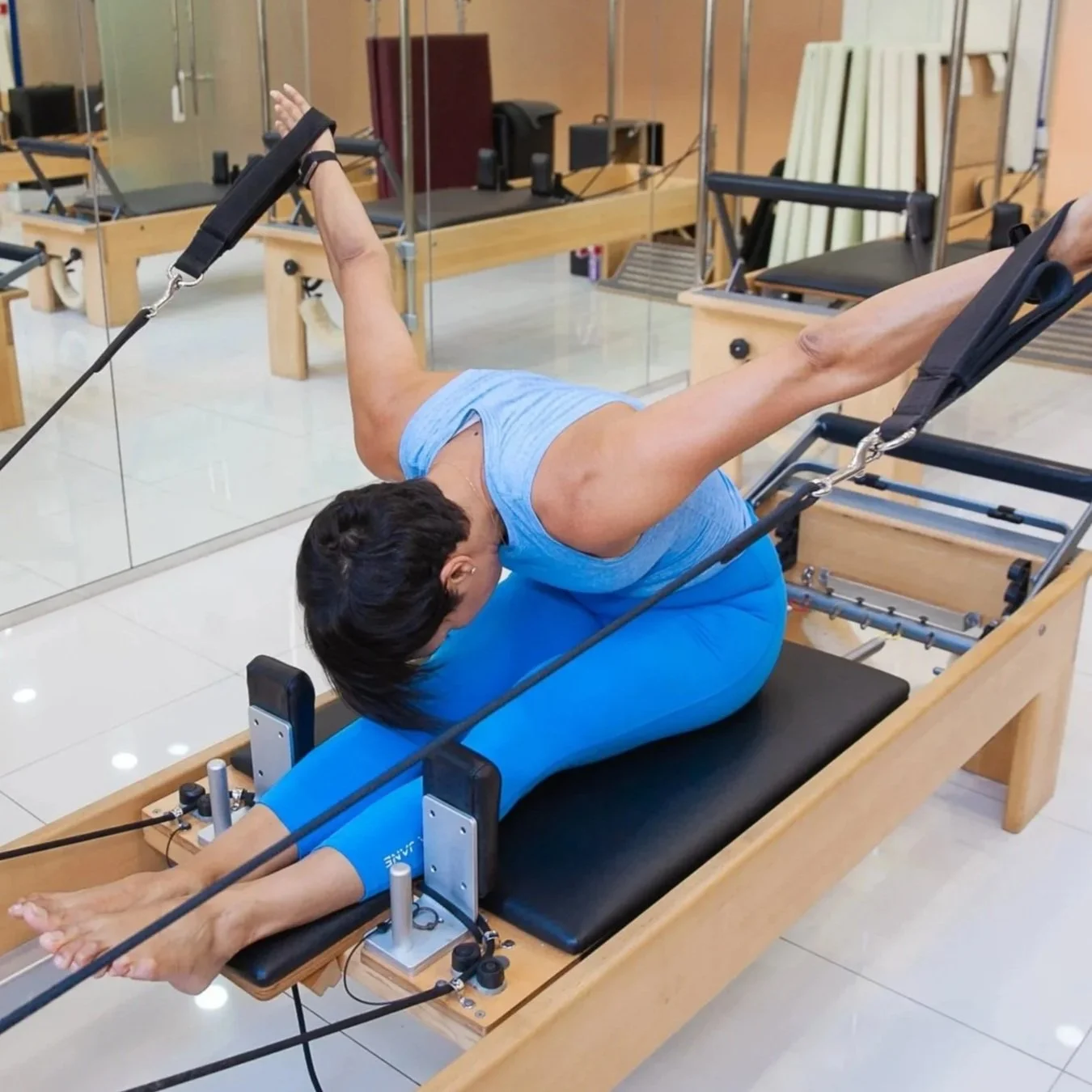 Paula Uribe performing an Pilates exercise on a reformer machine in a studio.