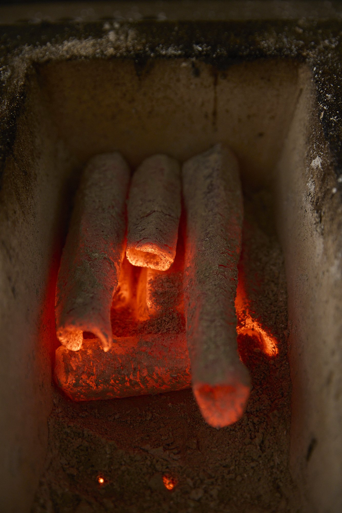 Close-up view of glowing burning incense sticks with ash and particles around them.