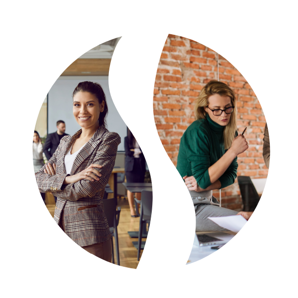 Two women in a professional setting, one smiling with arms crossed and the other looking at a document, with a brick wall background.