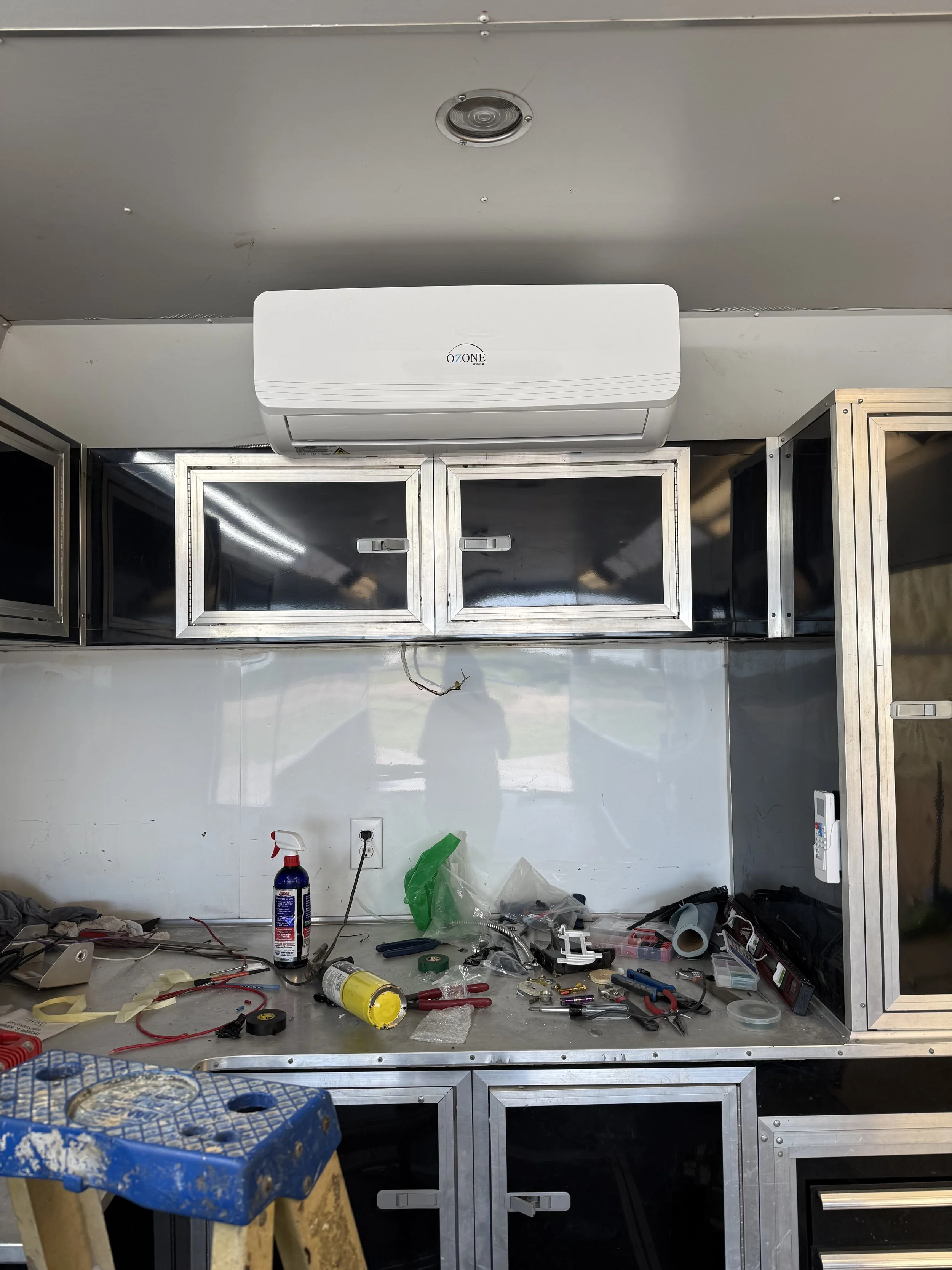 Workstation with tools, spray bottle, and containers on a metal countertop, upper wall-mounted cabinets, and an air conditioning unit.