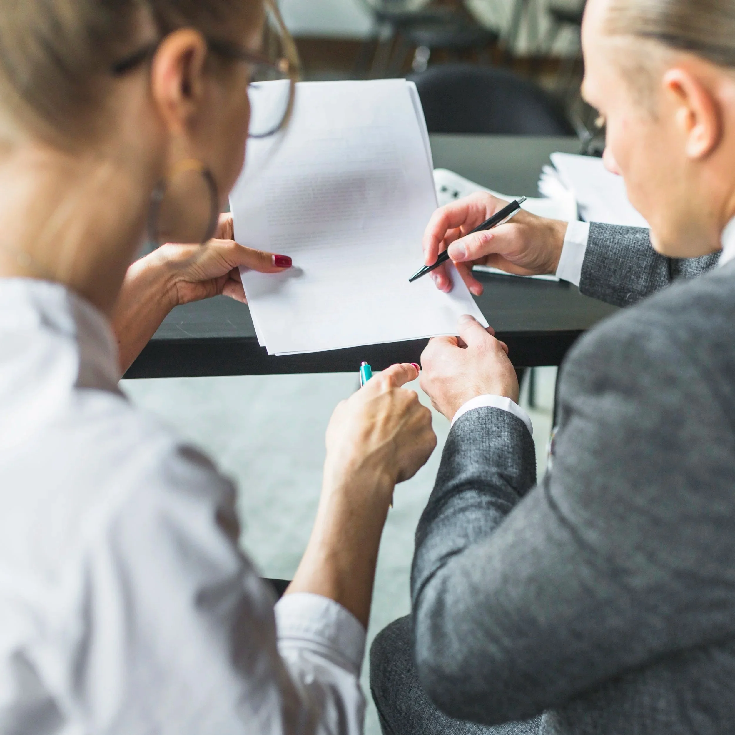 Two people reviewing documents together at a table, one holding a paper and the other pointing with a pen.
