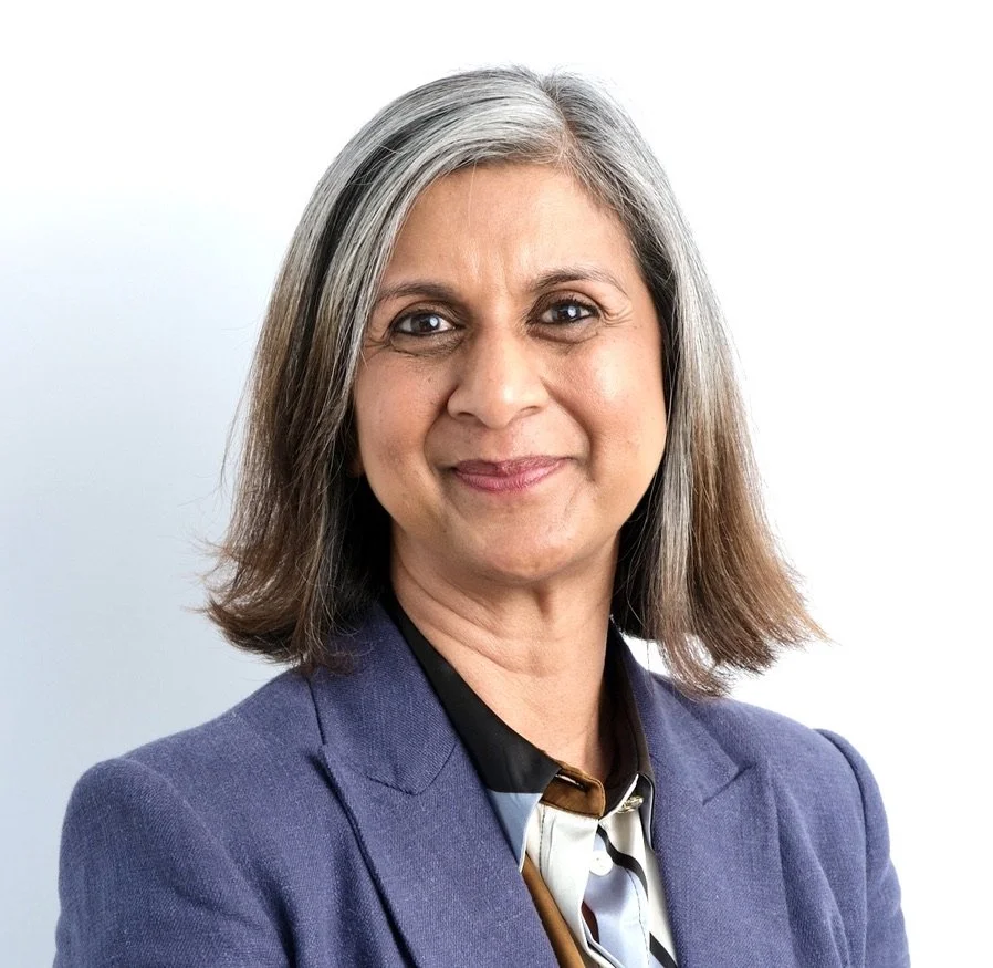 A professional woman with shoulder-length gray hair, wearing a dark blazer over a patterned blouse, smiling at the camera.