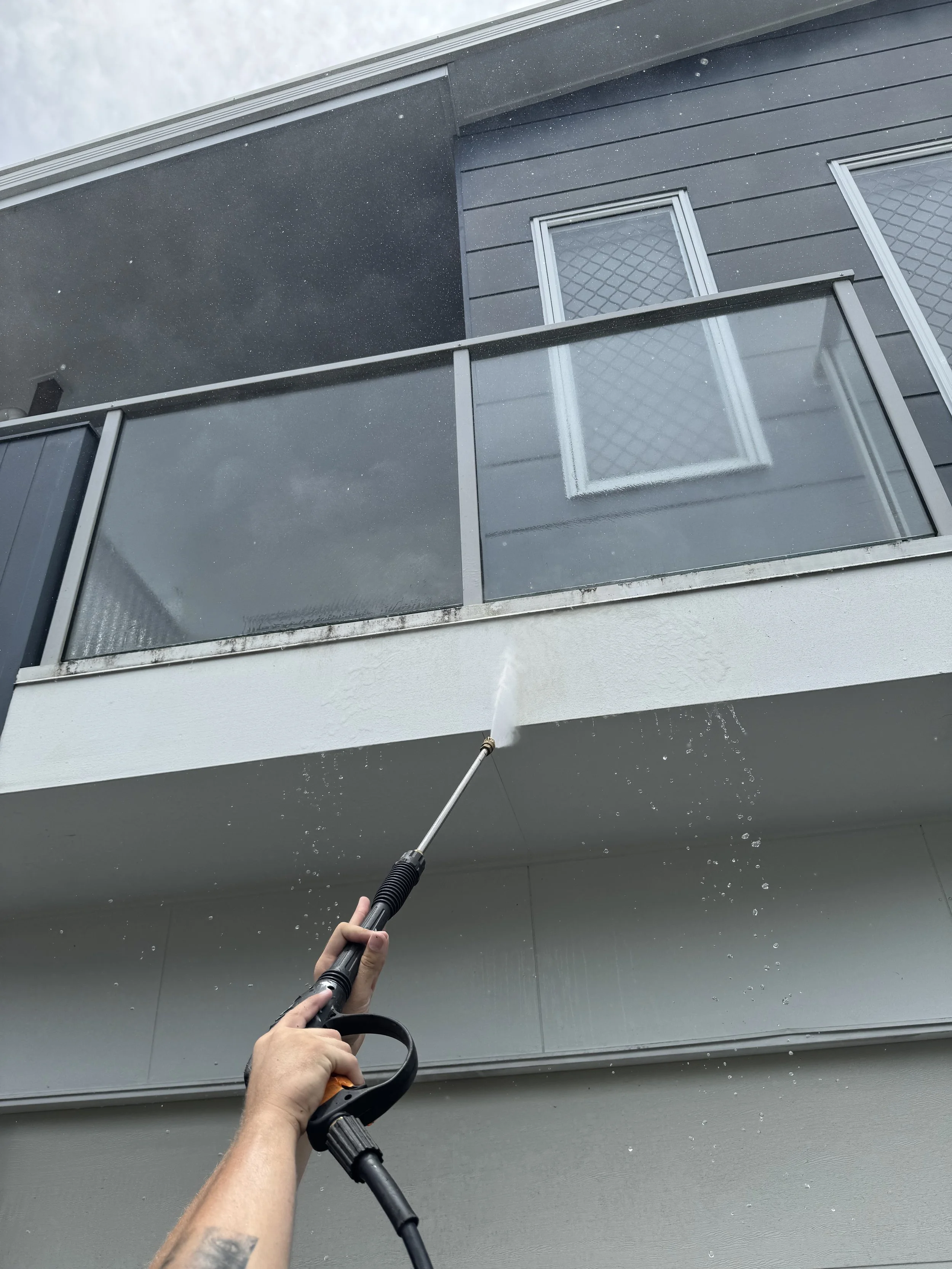 Person using a pressure washer to clean the underside of an outdoor balcony.