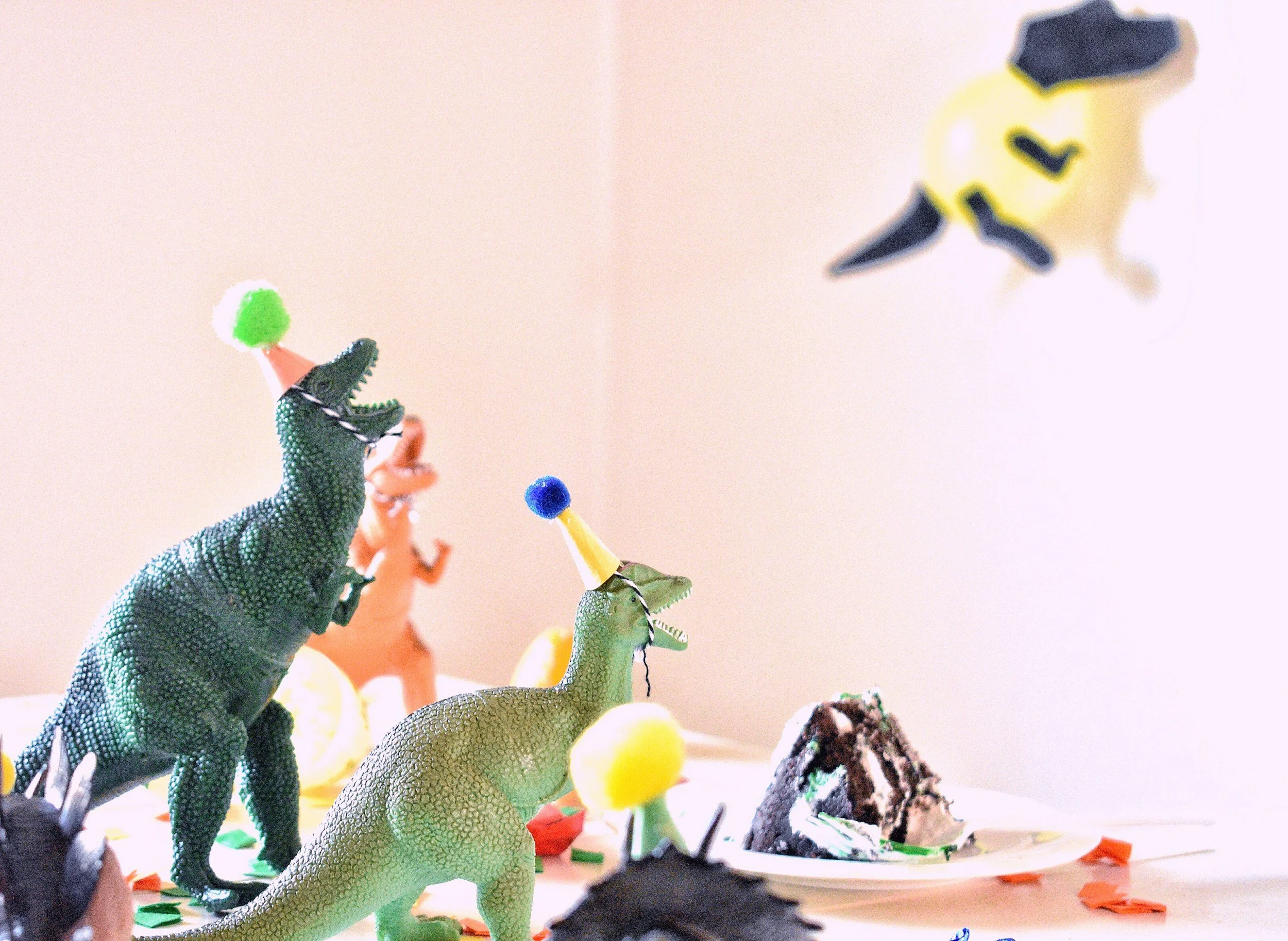 Toy dinosaurs with party hats and a cake on a table, celebrating a birthday.