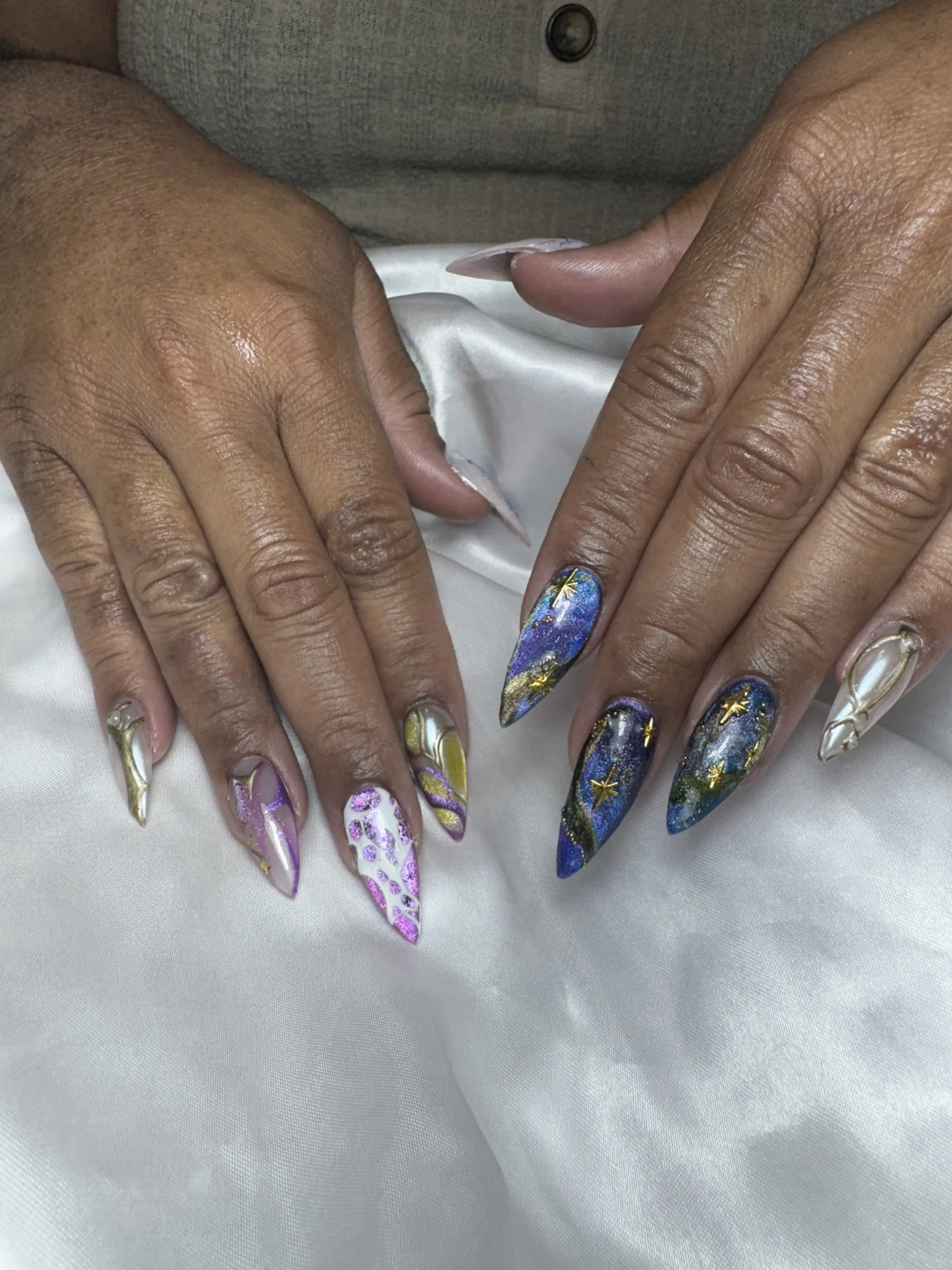 Close-up of hands with elaborate, colorful, galaxy-themed nail art on long, stiletto-shaped nails.