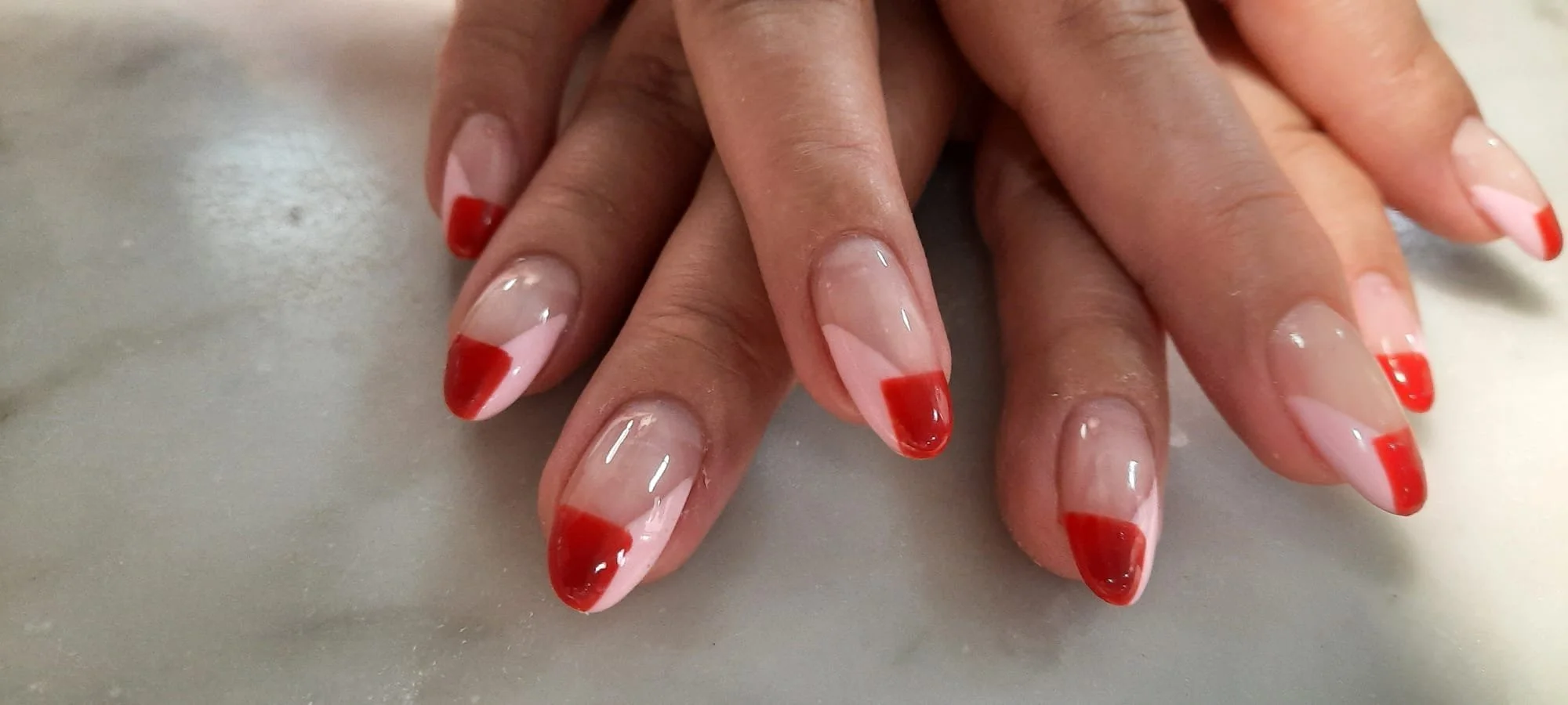 Close-up of hands with manicured nails featuring red French tips on natural nails.
