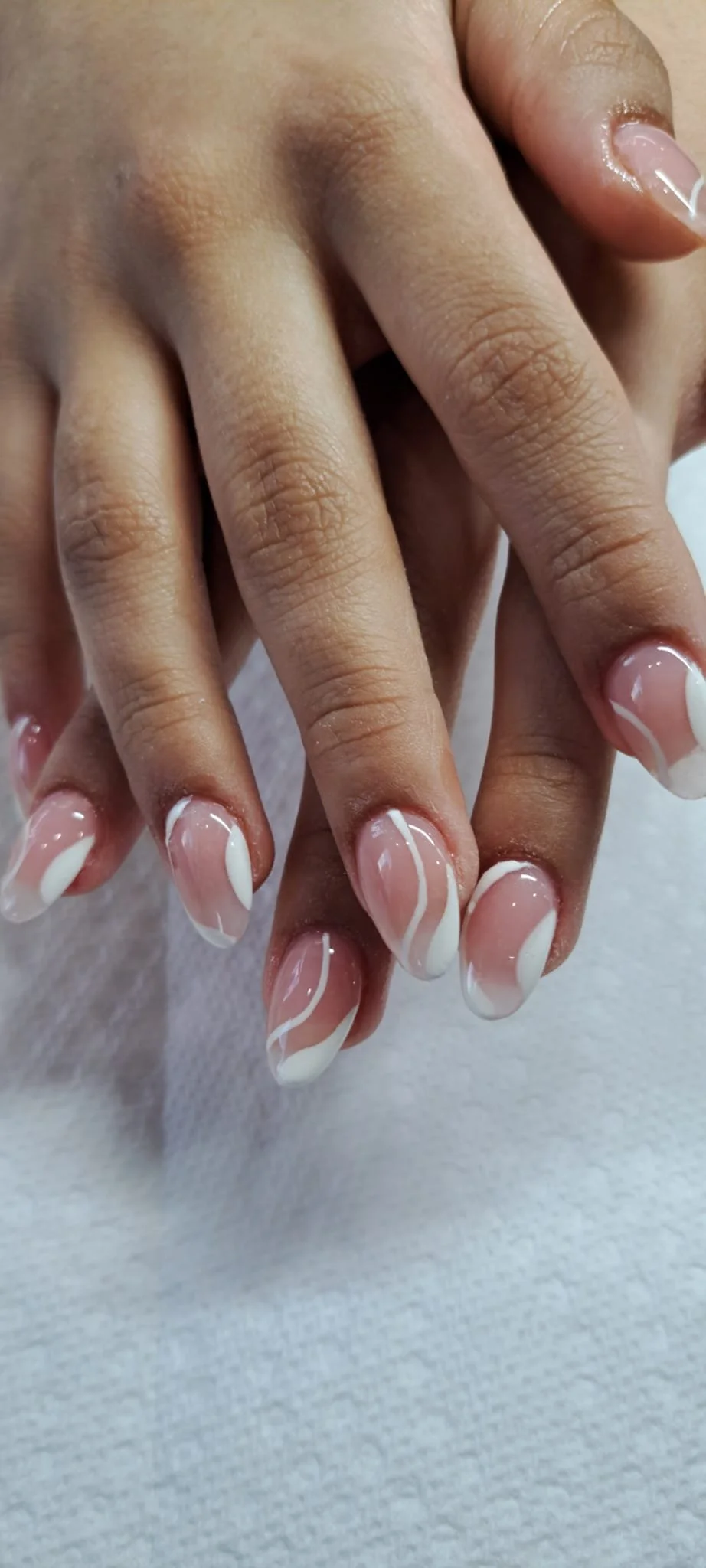 Close-up of a hand with neatly manicured nails featuring a pink base and white curved lines.