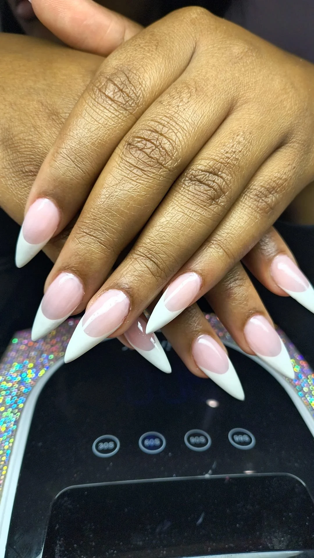 Close-up of hands with long, almond-shaped, French tip manicure resting on a digital device.