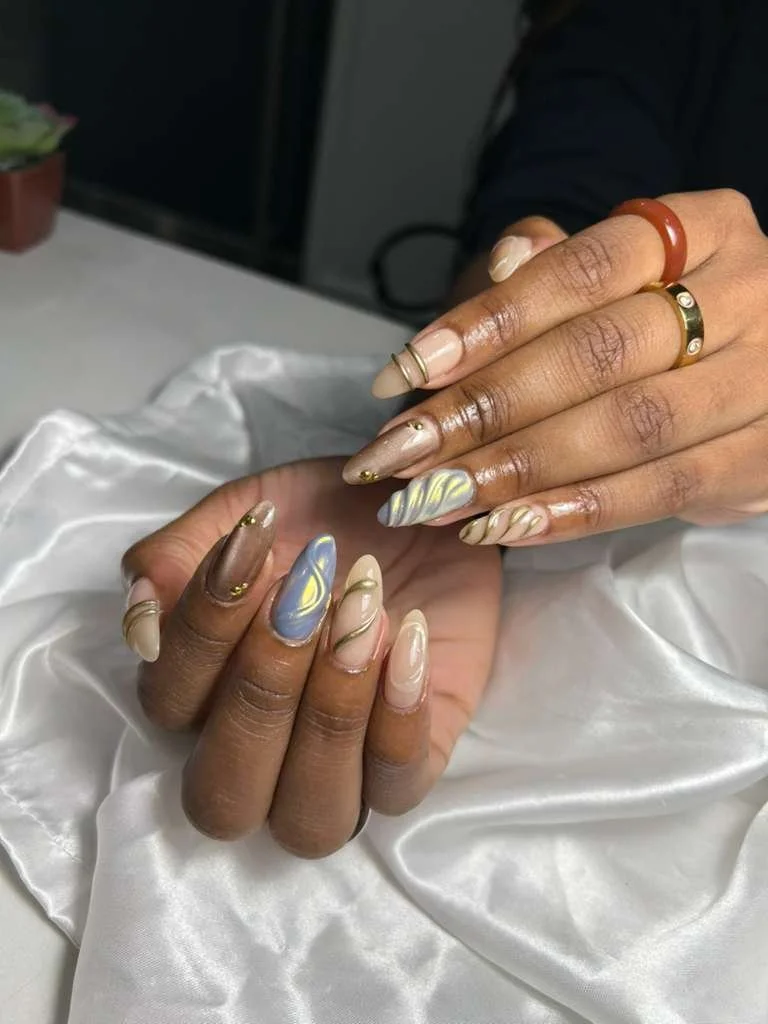 Close-up of two hands with manicured nails featuring marble and swirl designs in pastel shades, resting on a silky white fabric.