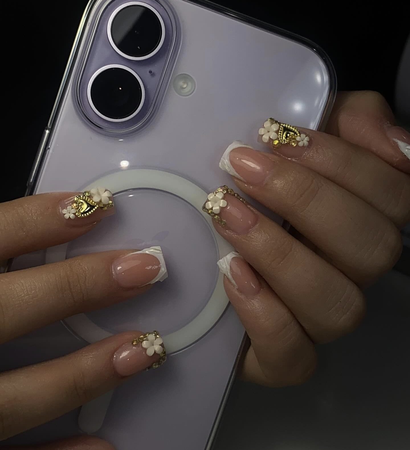 Close-up of a person's hand with decorated nails holding a smartphone with a magnetic ring grip.