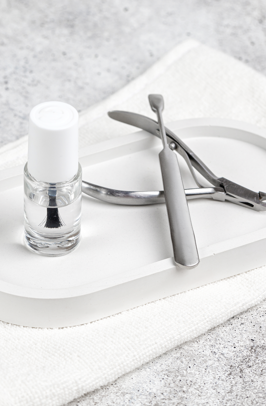 Nail polish remover, cuticle nippers, and a nail file on a white tray.