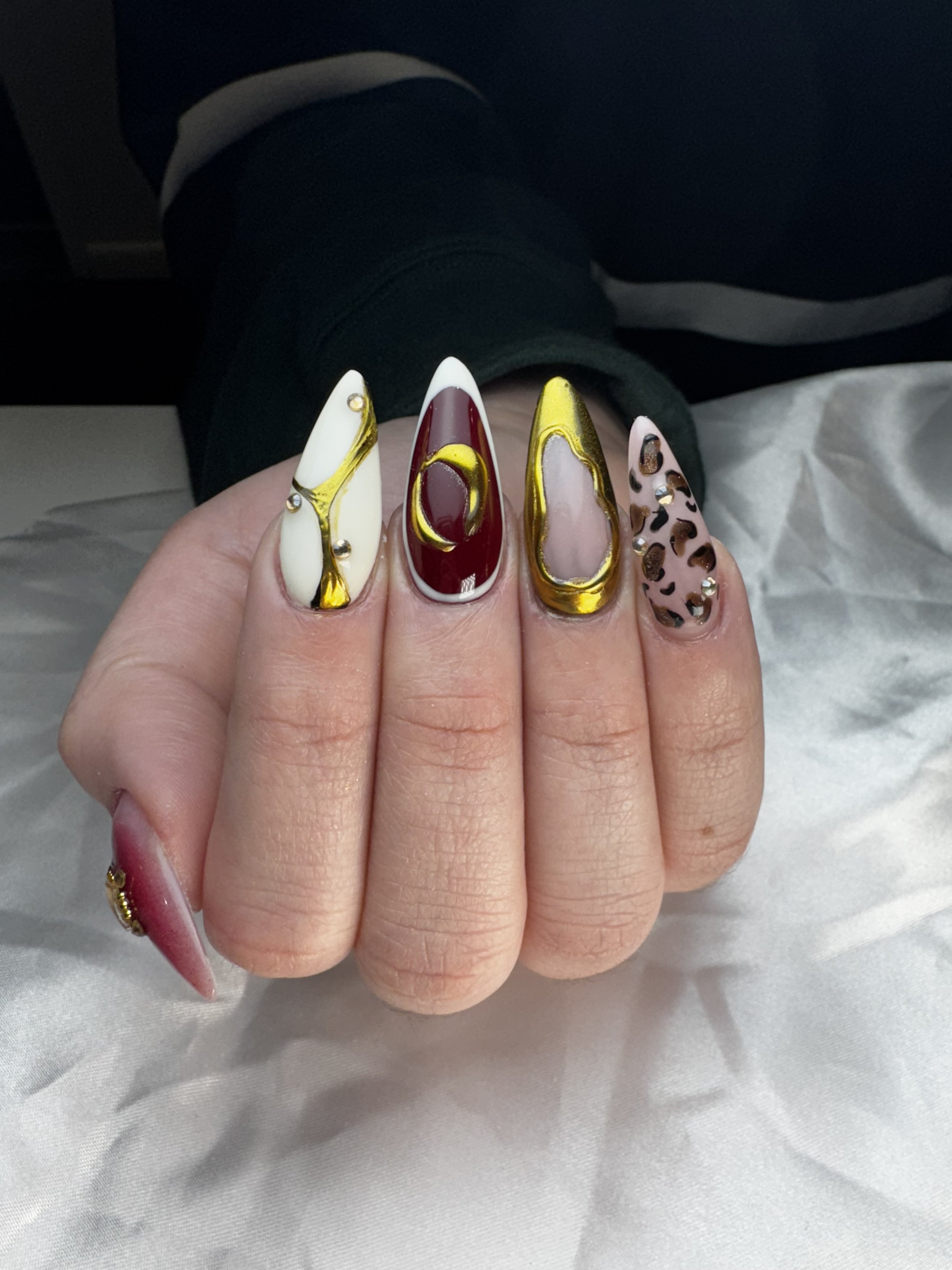 Close-up of a hand showing five decorated fingernails with various designs, including gold accents, rhinestones, and animal print patterns.