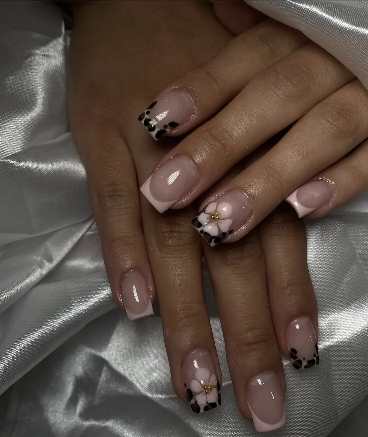 Close-up of hands with manicured nails; nails feature black and white leopard print tips with one nail decorated with a pink flower and gold accent.