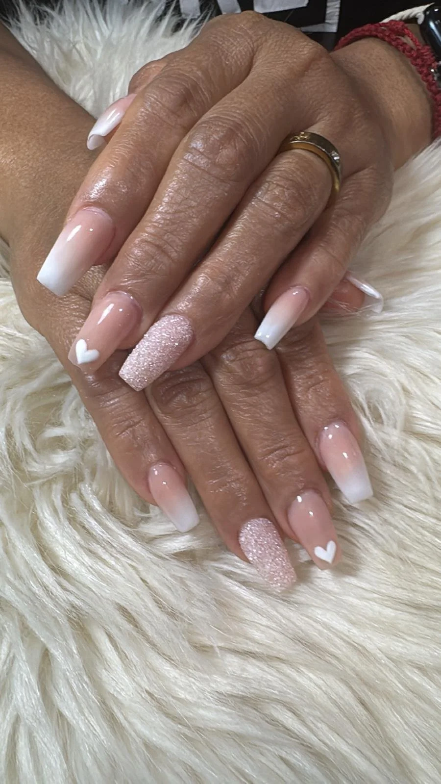 Close-up of a woman's hands showing manicured nails with French tips and heart designs, resting on a soft, cream-colored furry surface.