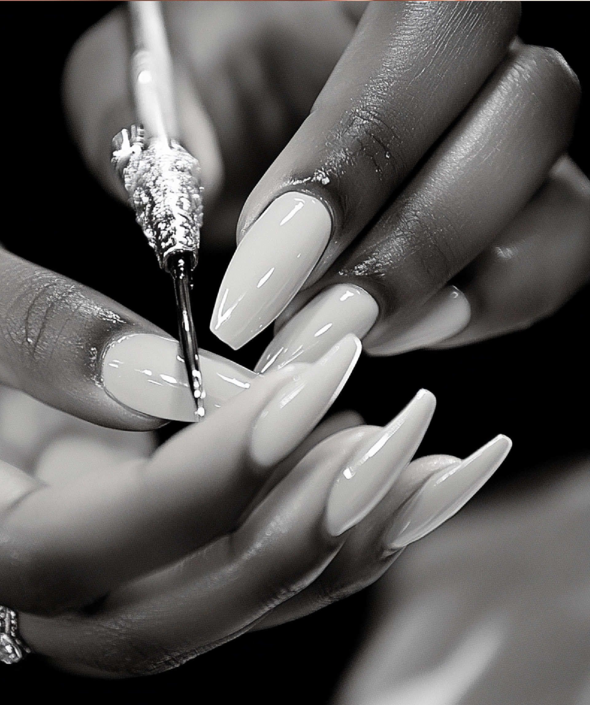 Close-up of a person painting or applying nail polish to their fingernails with a small brush, in black and white.