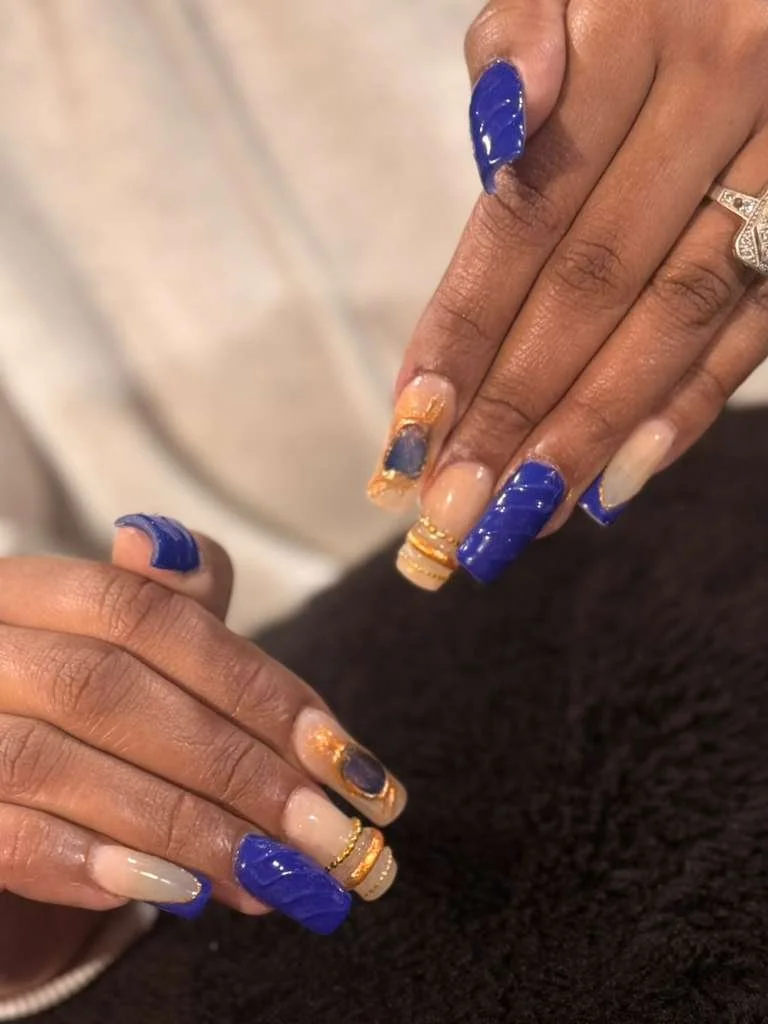 Close-up of hands with blue and beige nails, some adorned with gold accents and rings.