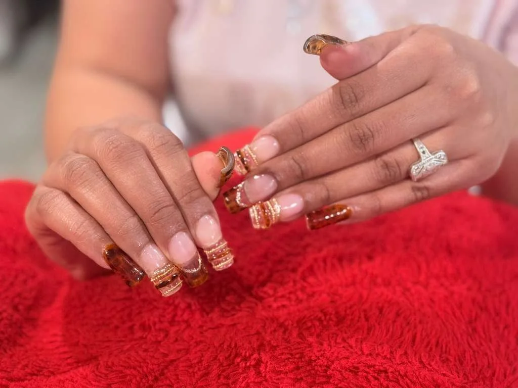 Close-up of female hands with manicured nails and jewelry, resting on a red textured fabric.
