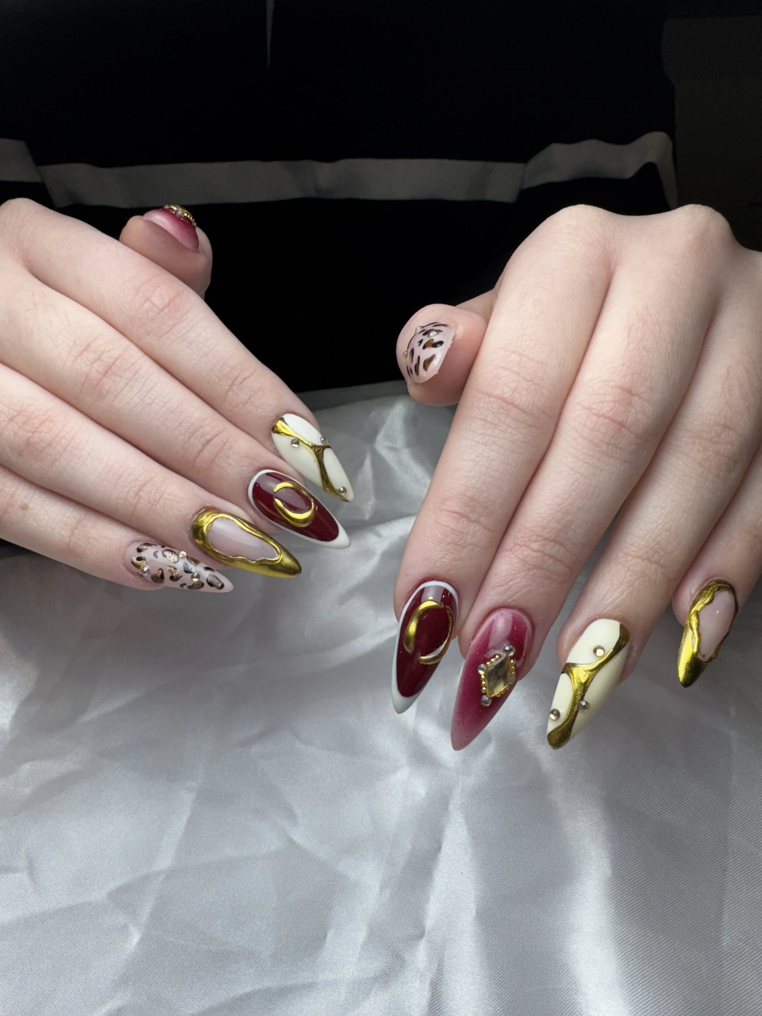 Close-up of two hands with elaborate, artistic nails featuring red, white, gold, black, and leopard print designs.