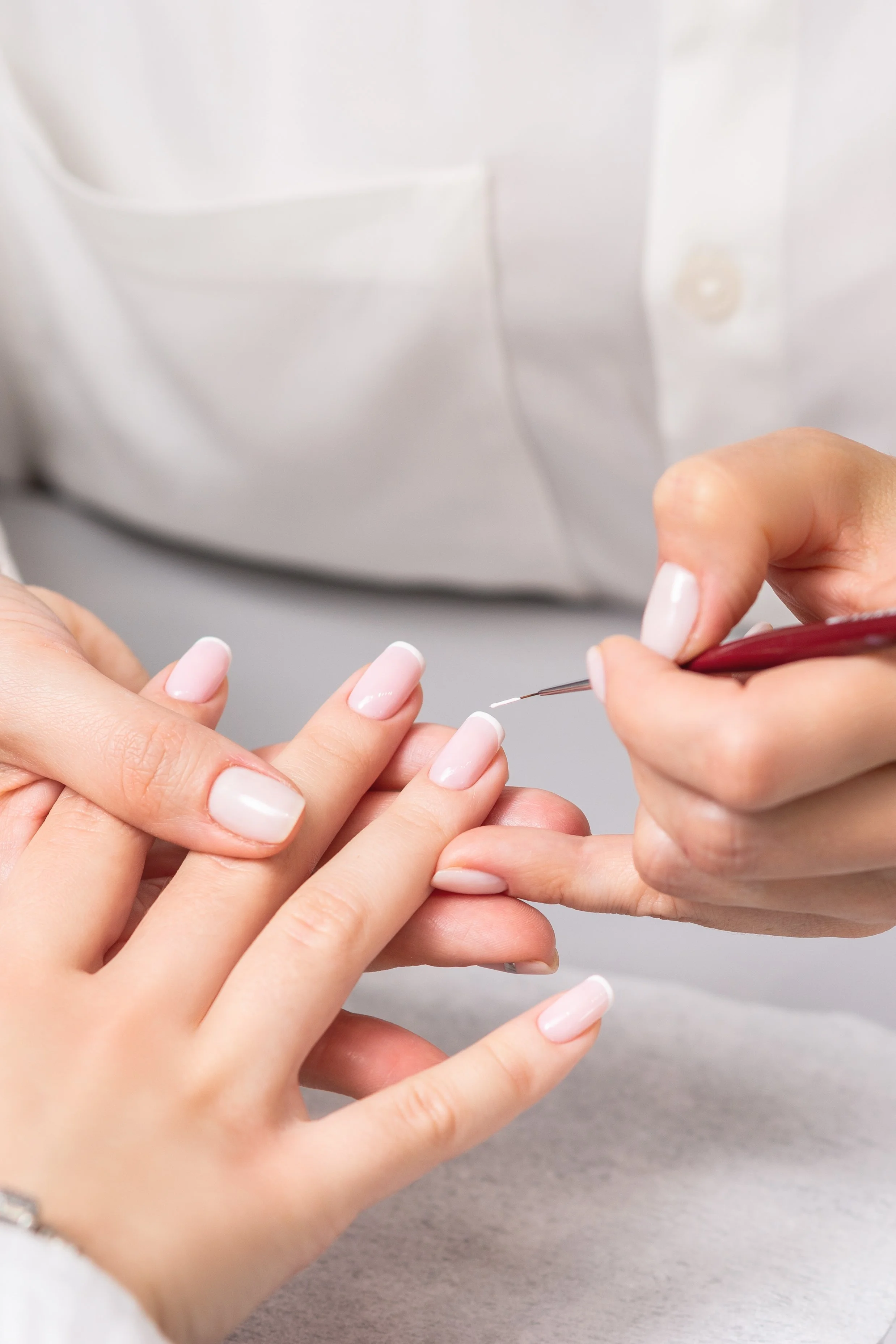 A manicurist applying clear nail polish to a client's fingernails.