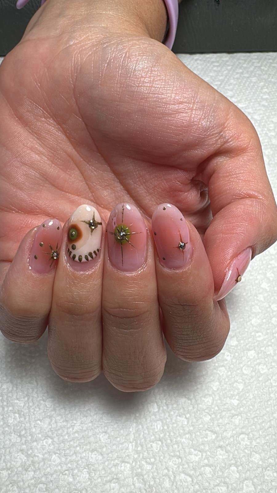 Close-up of manicured nails with pink and white gradient polish, decorated with small rhinestones and star-shaped metallic accents.
