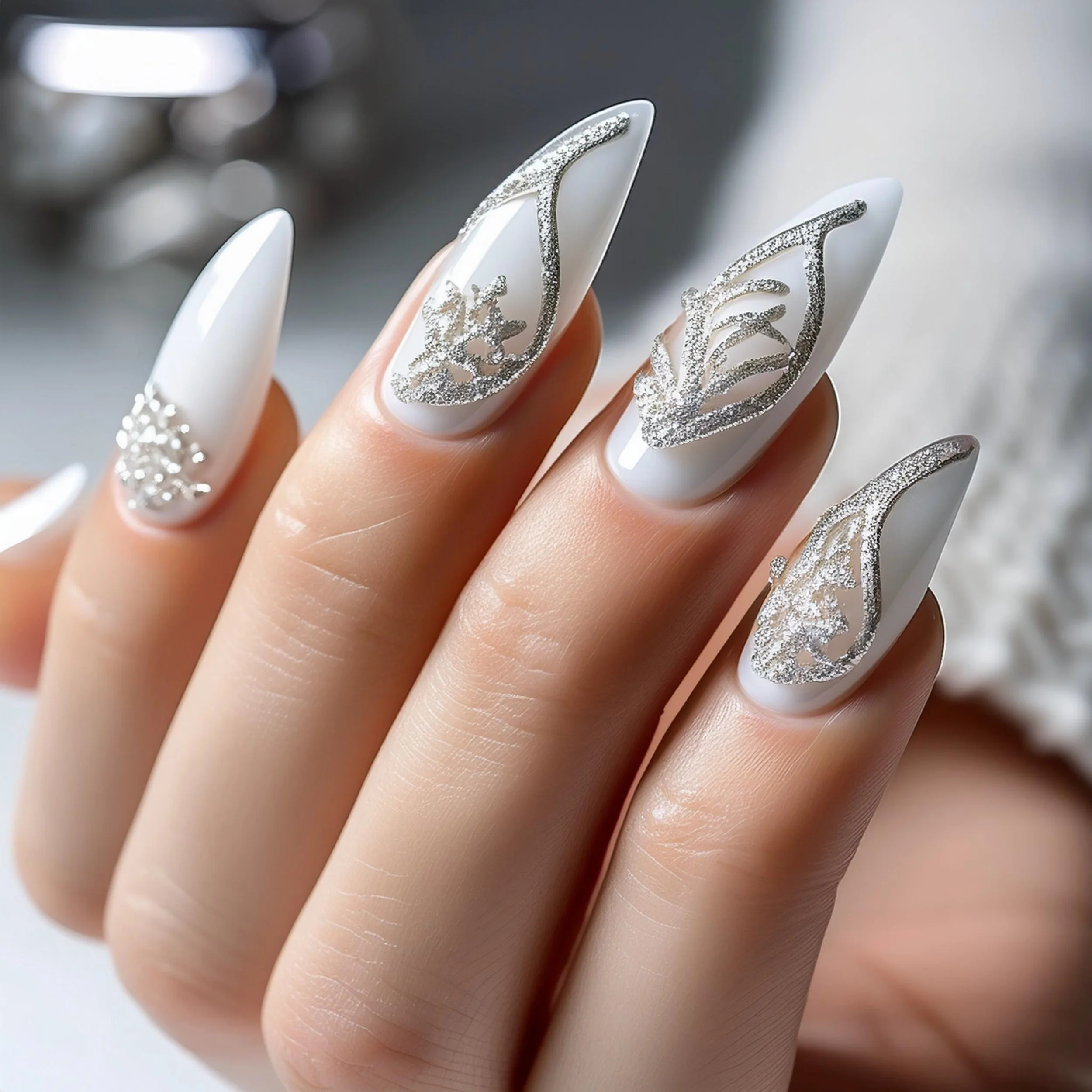 Close-up of a hand with long, white almond-shaped nails featuring silver glitter and intricate silver lace designs.