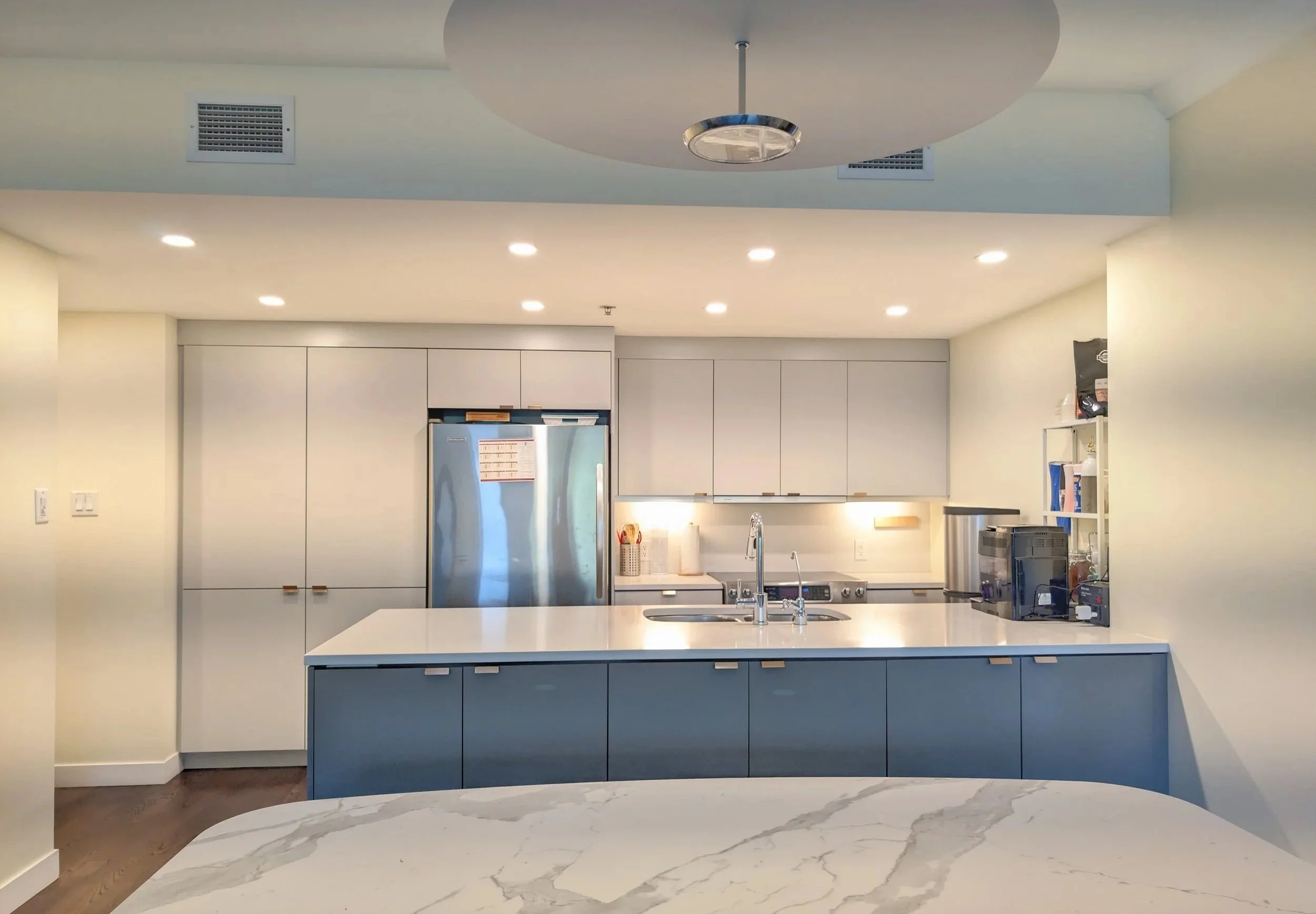 Modern kitchen with white cabinets, a large island with a blue base, stainless steel appliances, and a marble countertop in an apartment or hotel suite.