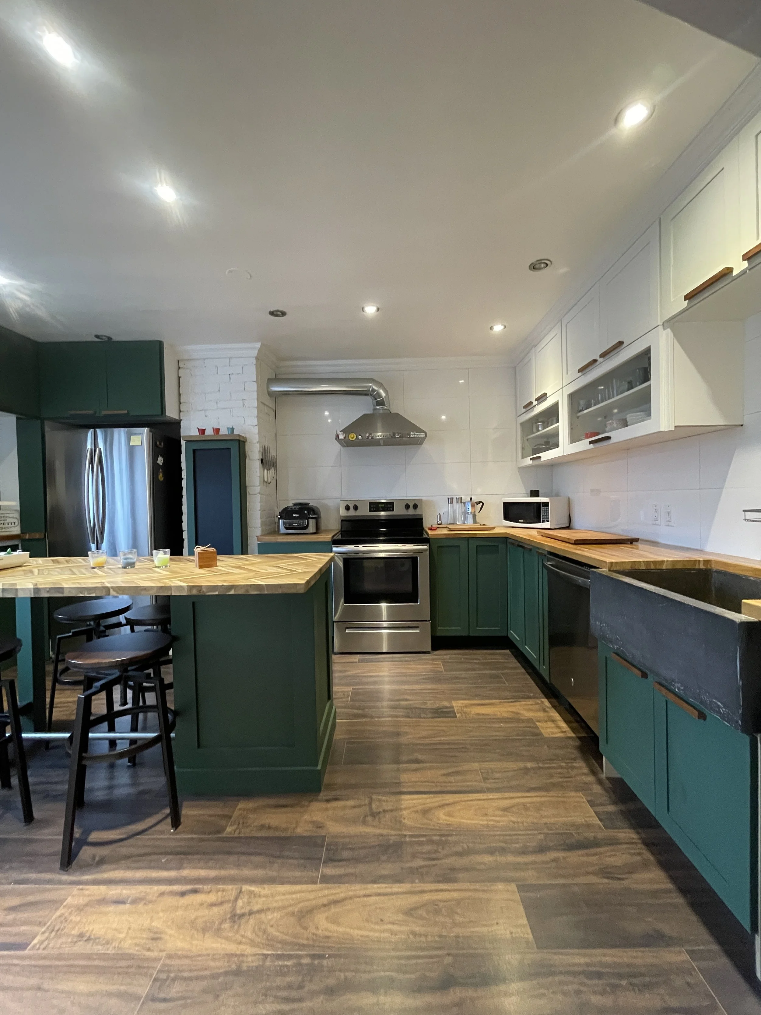 Kitchen with green cabinets, a wooden island, stainless steel appliances, white upper cabinets with glass doors, and wood flooring.