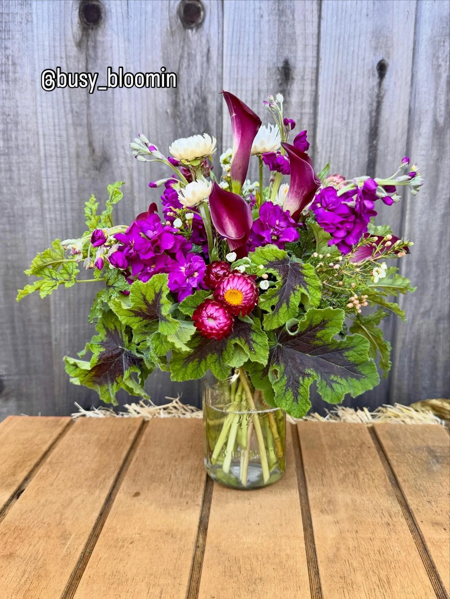 Vibrant purple and green hand-tied floral bouquet in a clear glass vase.