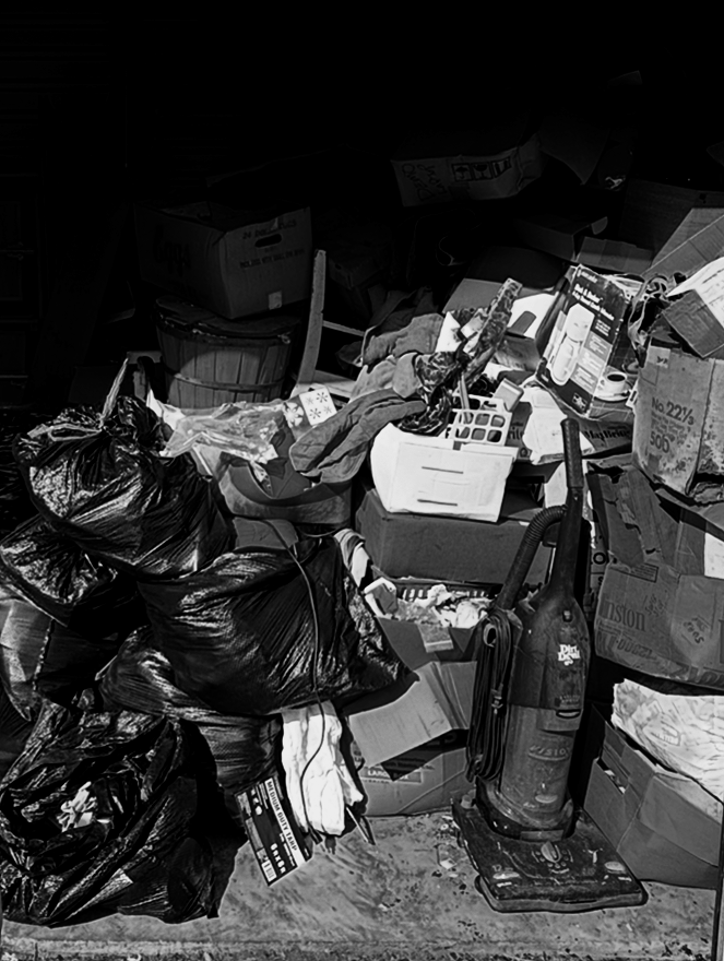 Cluttered storage space with black trash bags, boxes, and a vacuum cleaner.