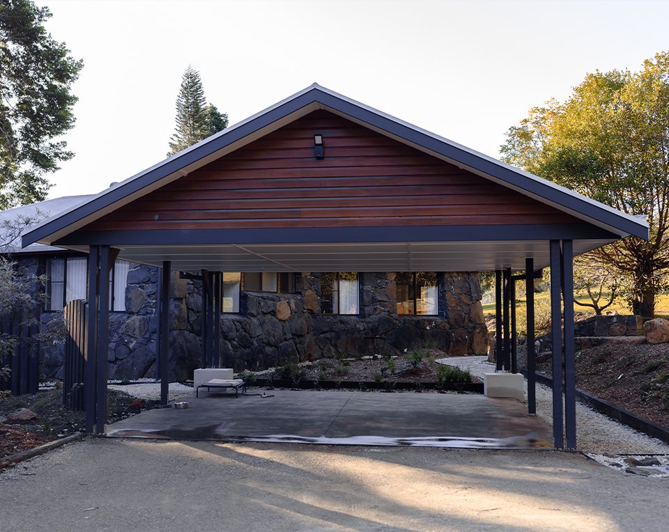 A modern house with a carport, stone and wood exterior, and surrounding trees.