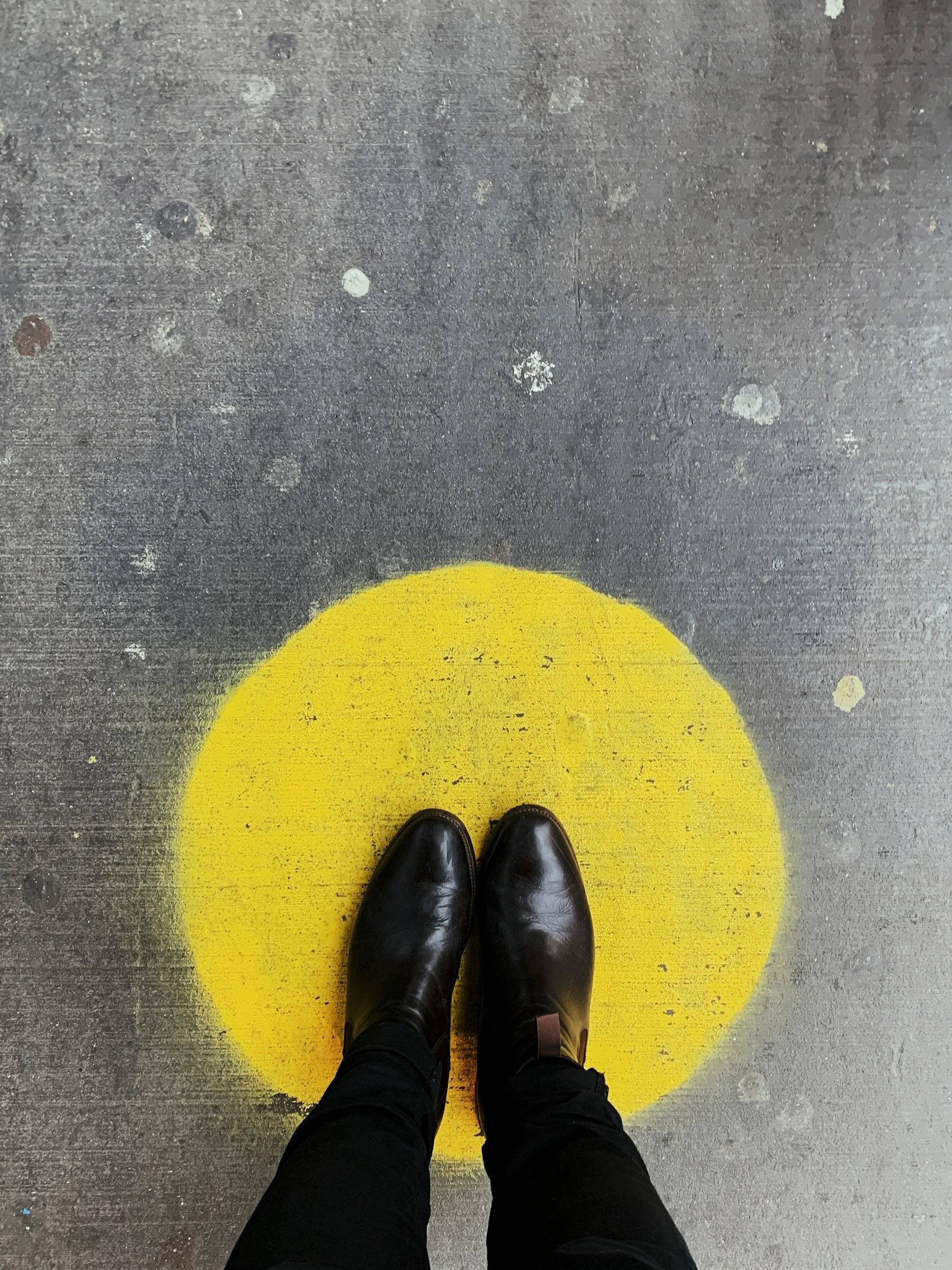 Person standing on a concrete floor with a yellow circle painted on the ground beneath their black shoes.