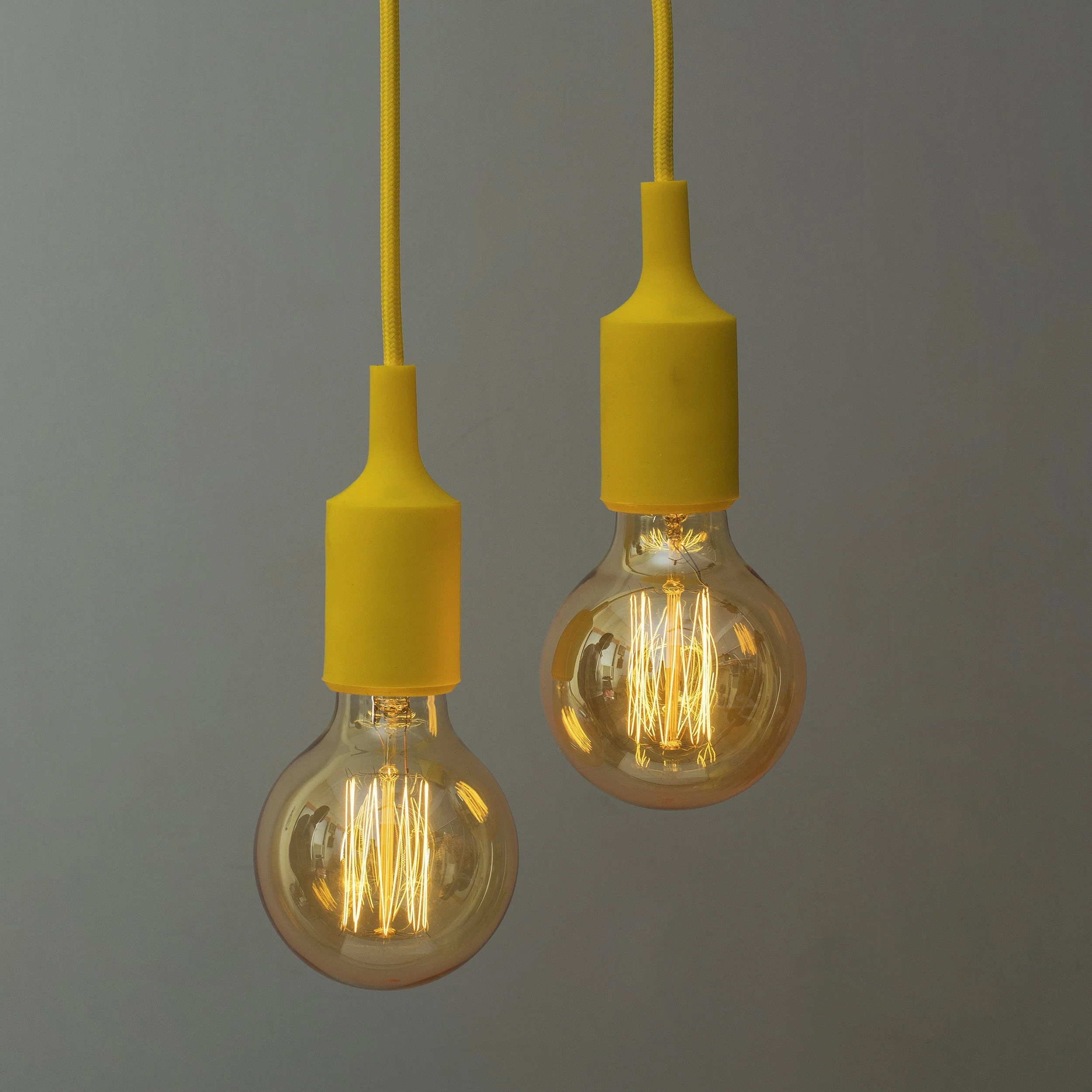 Two hanging yellow pendant light bulbs with filament designs glowing against a gray wall.