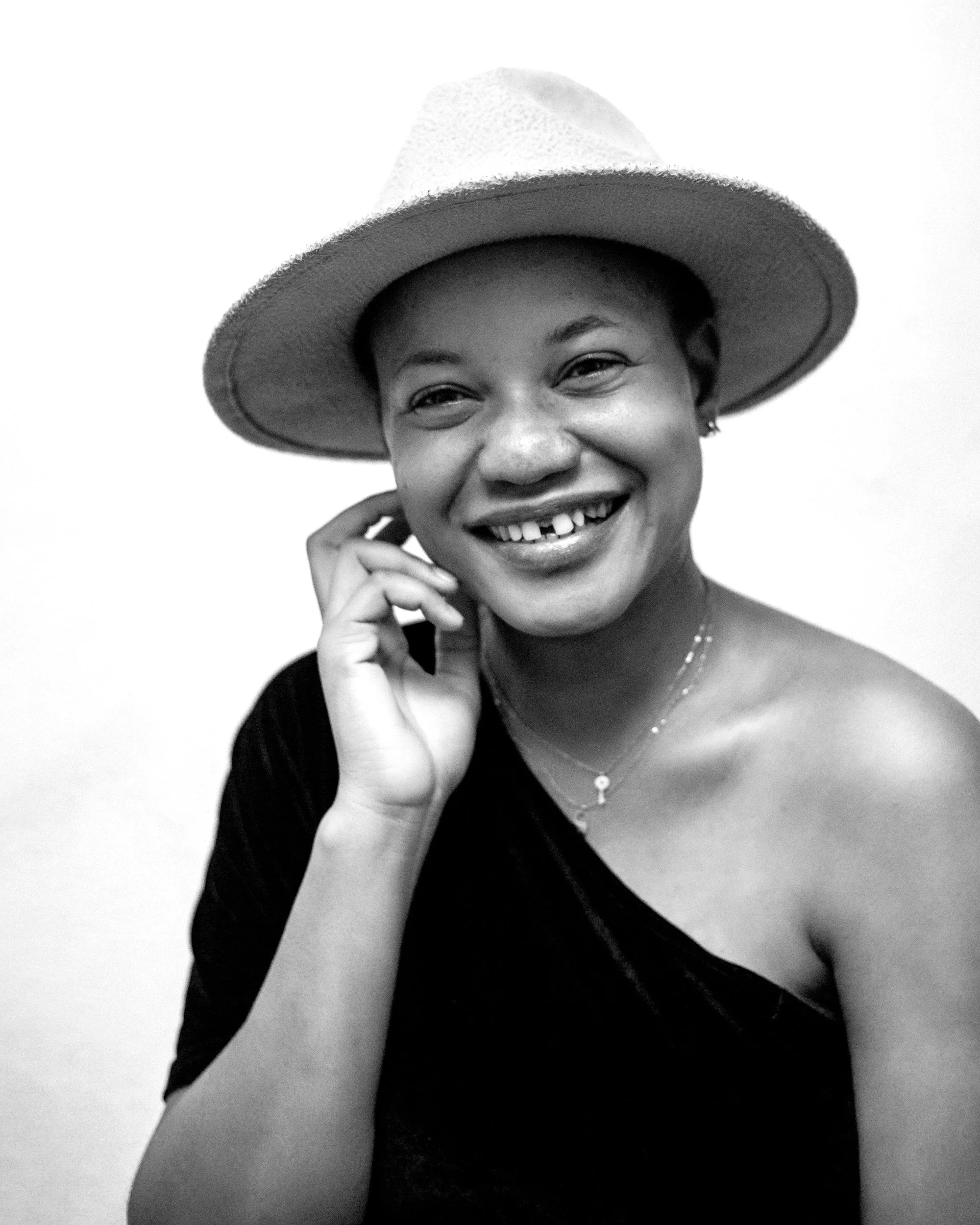 Smiling woman wearing a wide-brimmed hat and a black top, with jewelry, in black and white.